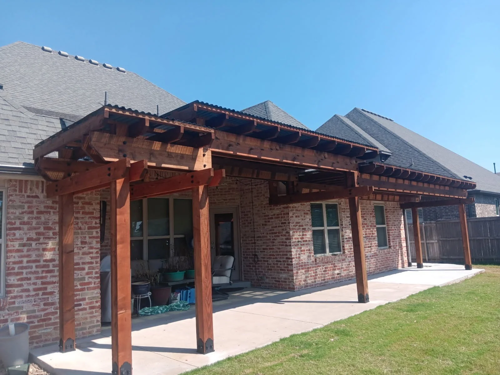 Backyard with a brick house, wooden patio cover, and outdoor furniture during daytime.