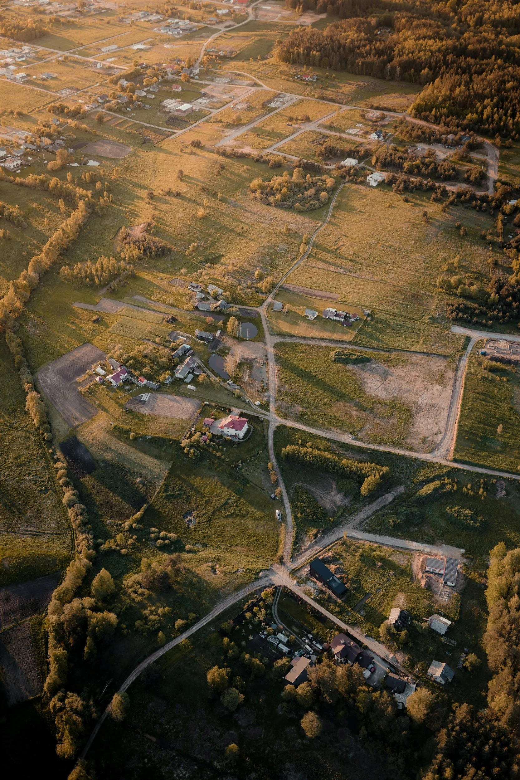 Aerial view of a rural landscape with scattered houses, roads, trees, and fields during sunset or sunrise.