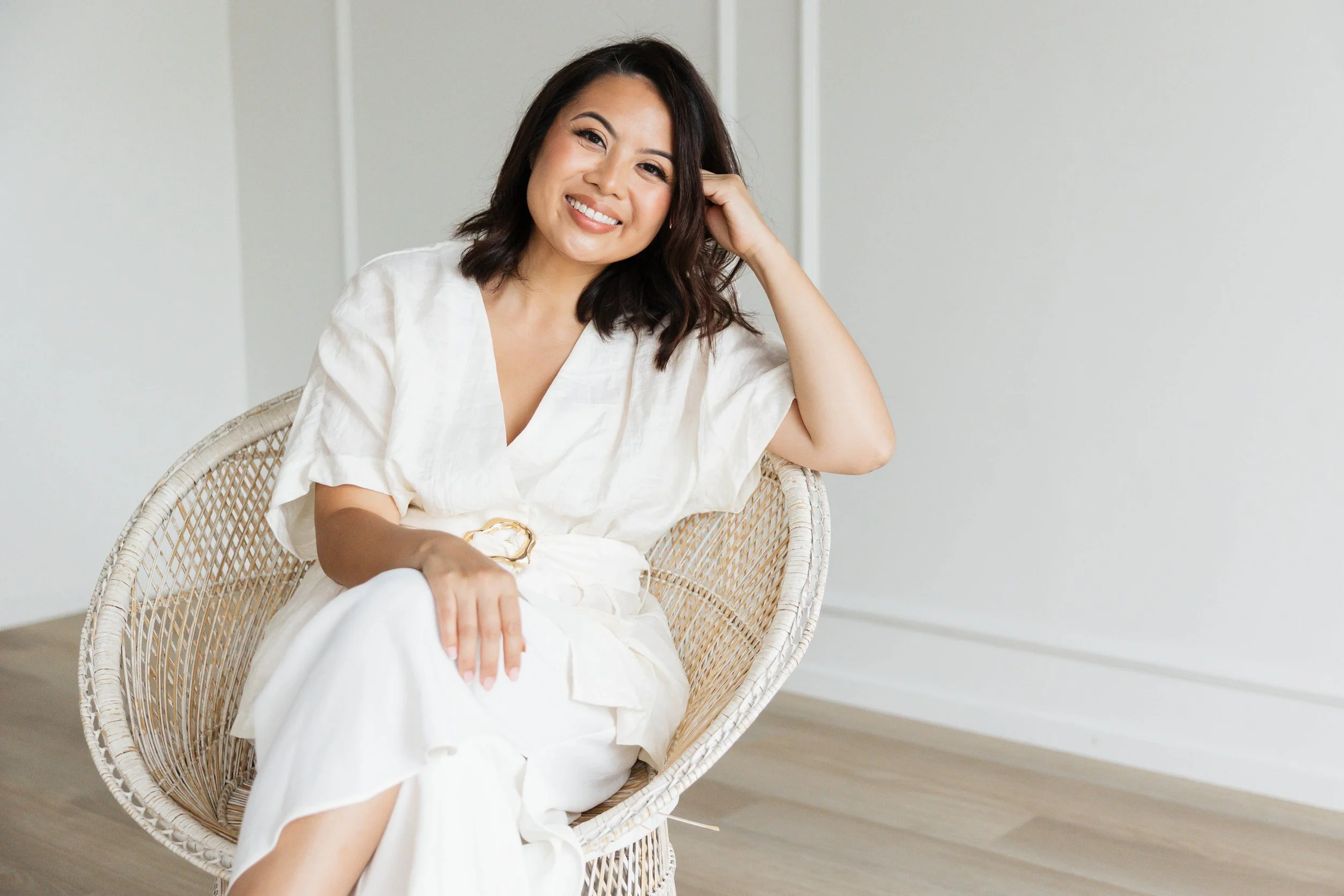 Kristine Allen, founder of MILA Co Advisory, smiling and sitting in a woven chair. A woman with medium-length dark hair in a white outfit, representing her hospitality consulting brand.