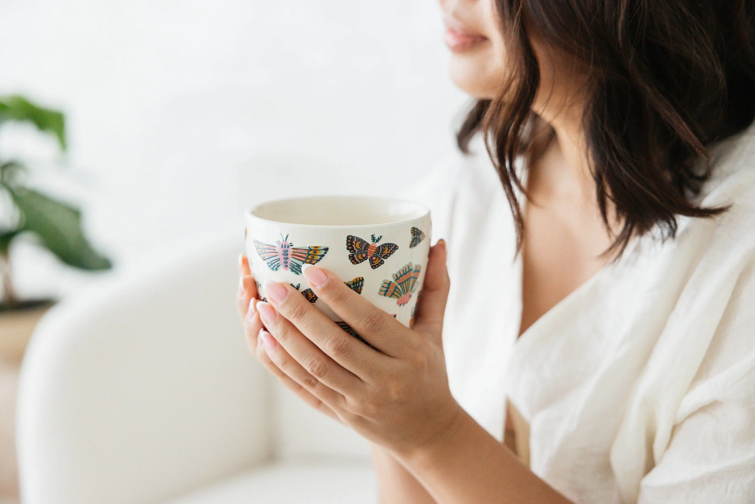 Kristine Allen, founder of MILA Co Advisory, holding a white mug with colorful butterflies close to her face. A warm, candid portrait highlighting the personal hospitality values behind her consulting brand.