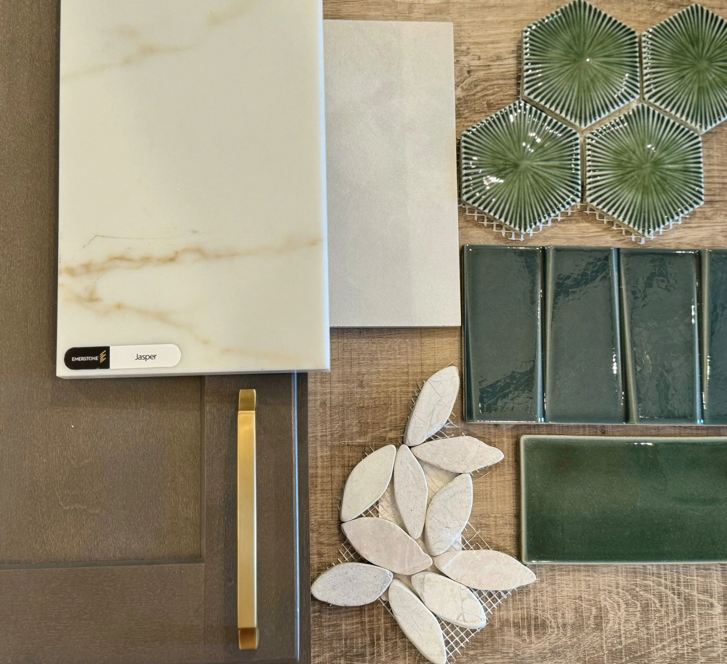 Samples of various tiles and marble slabs, including green hexagonal tiles with sunburst pattern, beige stone tiles, and patterned marble slabs, displayed on a wooden surface.