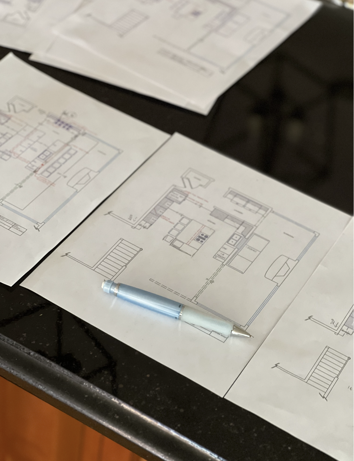 Architectural blueprints and floor plans on papers placed on a black surface with a light blue pen in front.