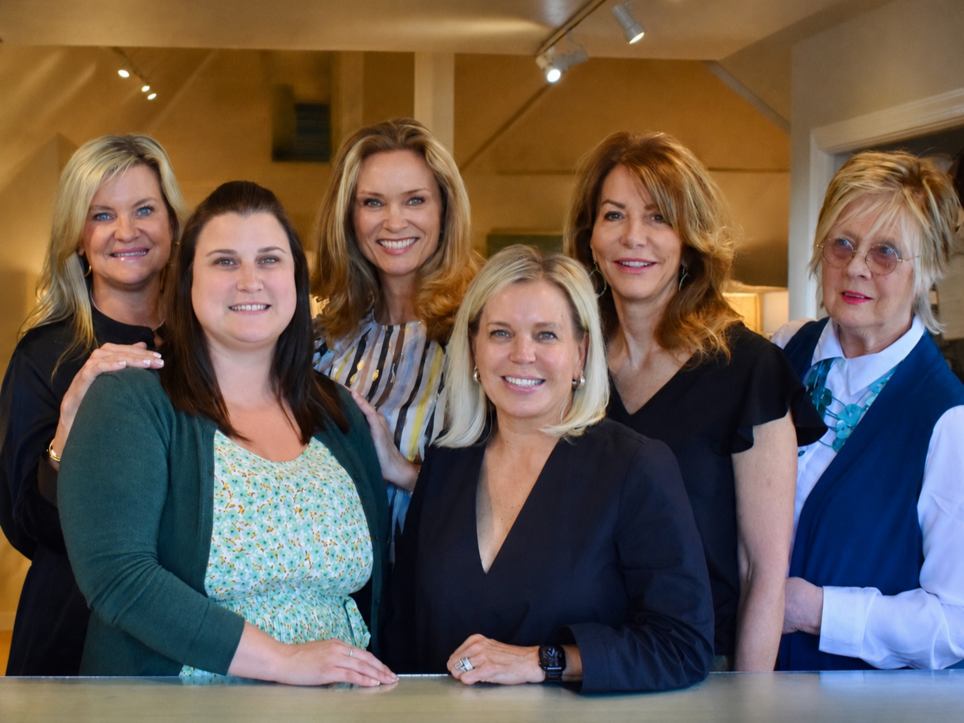 Group of seven women posing together indoors, smiling at the camera.
