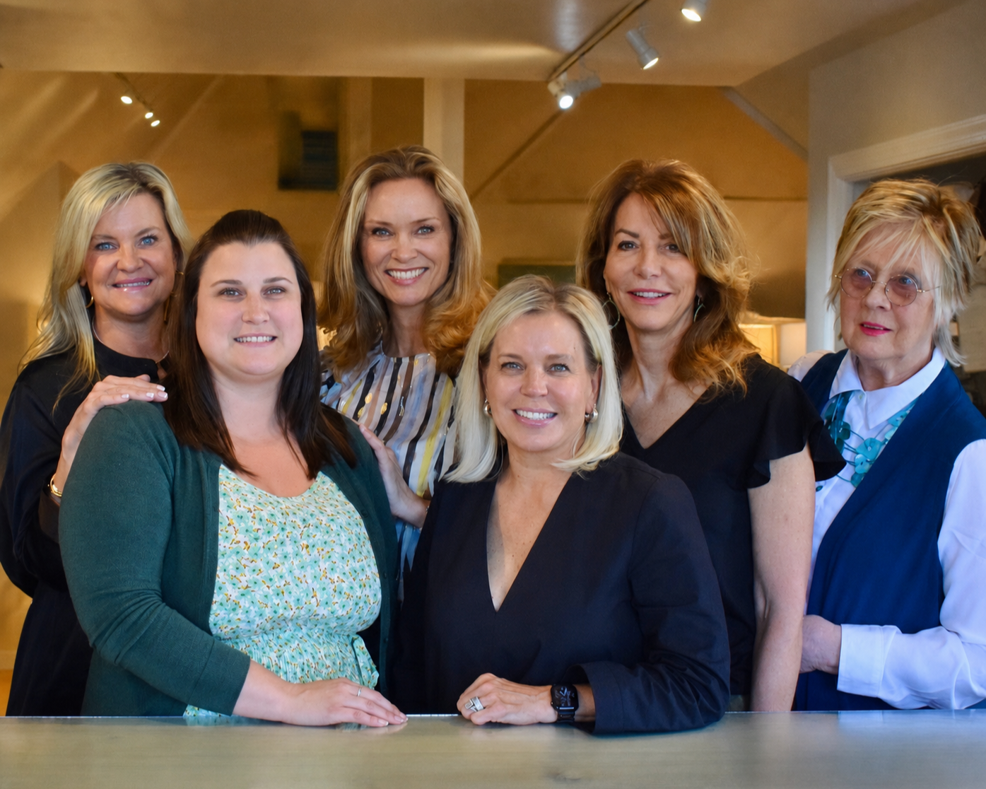 A group of seven women smiling and posing together in an indoor setting.