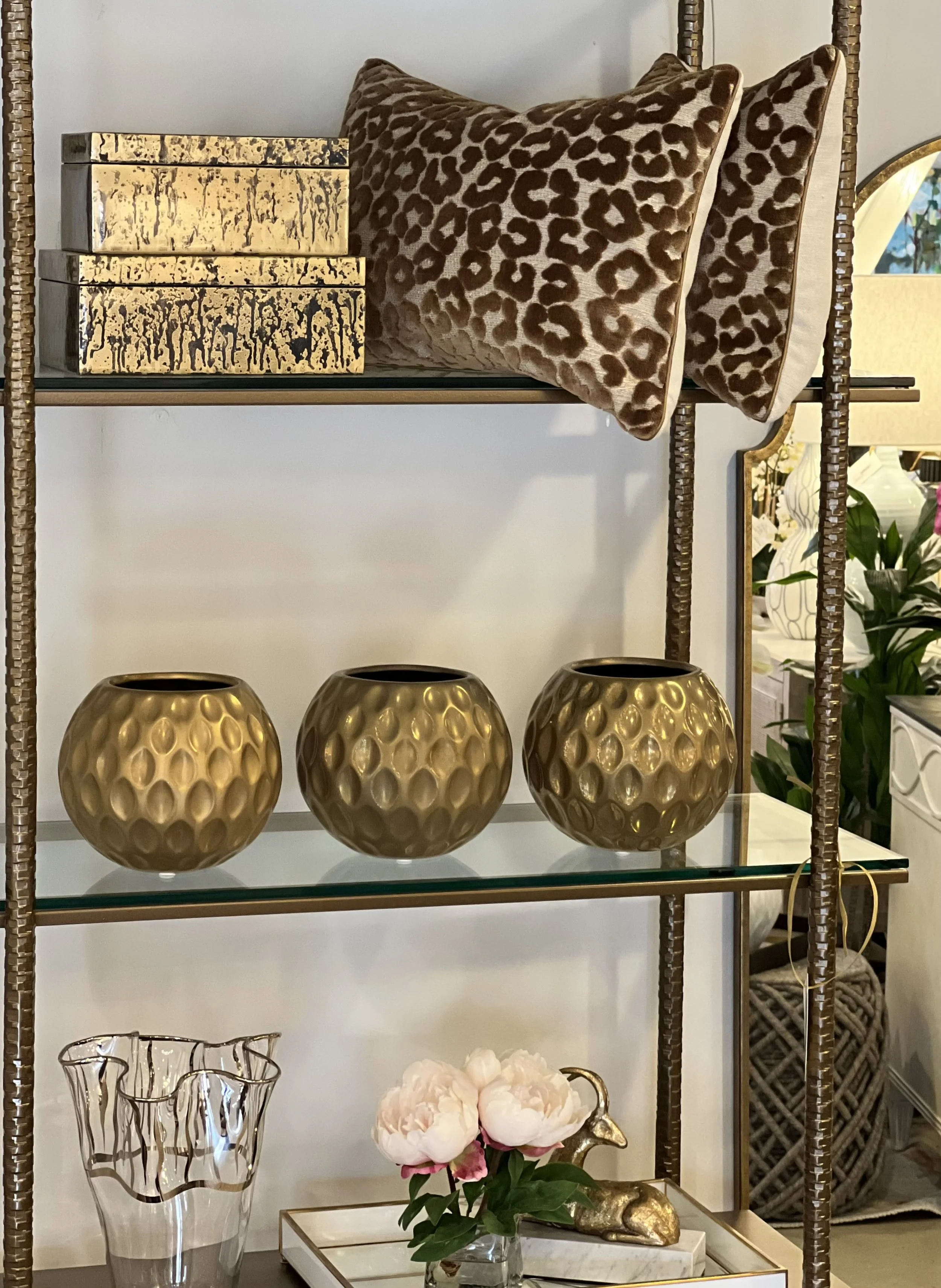 Decorative interior shelf displaying gold-colored vases, leopard print pillows, and various decorative items including a glass vase with metallic accents, a white marble tray with pink flowers, and a gold rabbit sculpture.