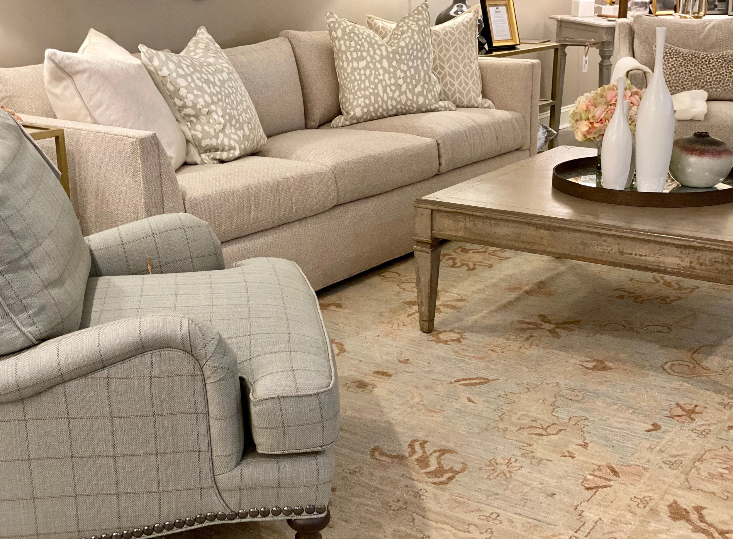 Living room with beige sofa and patterned pillows, coffee table with vases and flowers, and a patterned rug.