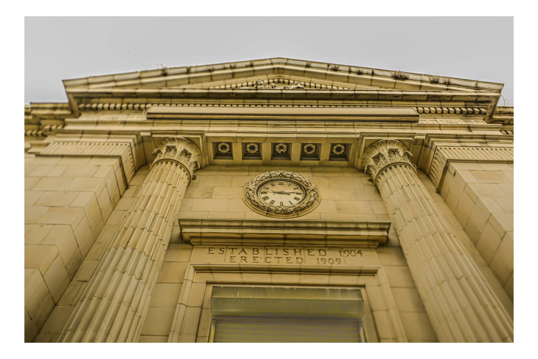 Upward view of a historic building with classical columns and a clock, with inscriptions indicating it was established in 1904 and reconstructed in 1909.