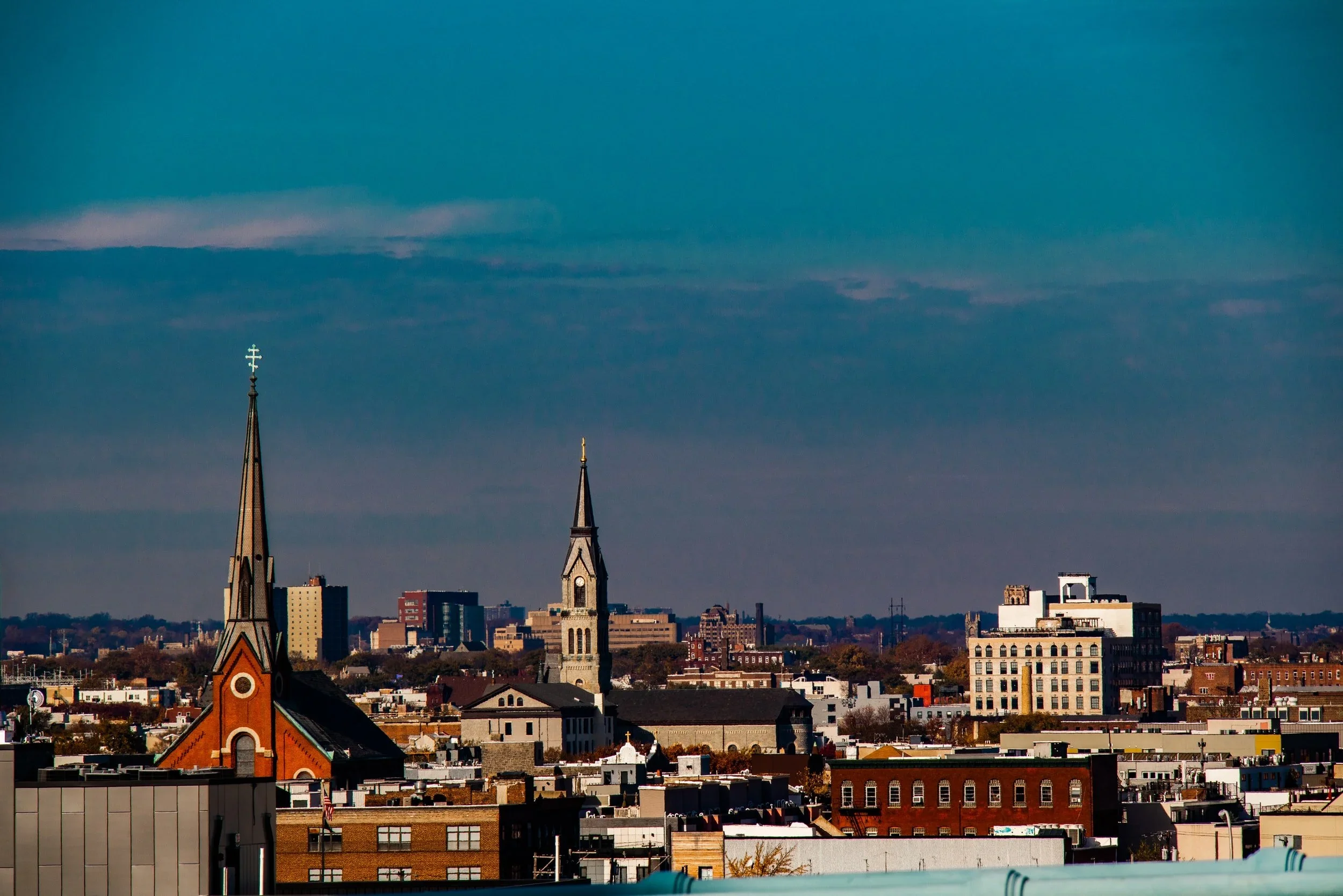 City skyline with church steeples, tall buildings, and a blue sky with clouds.