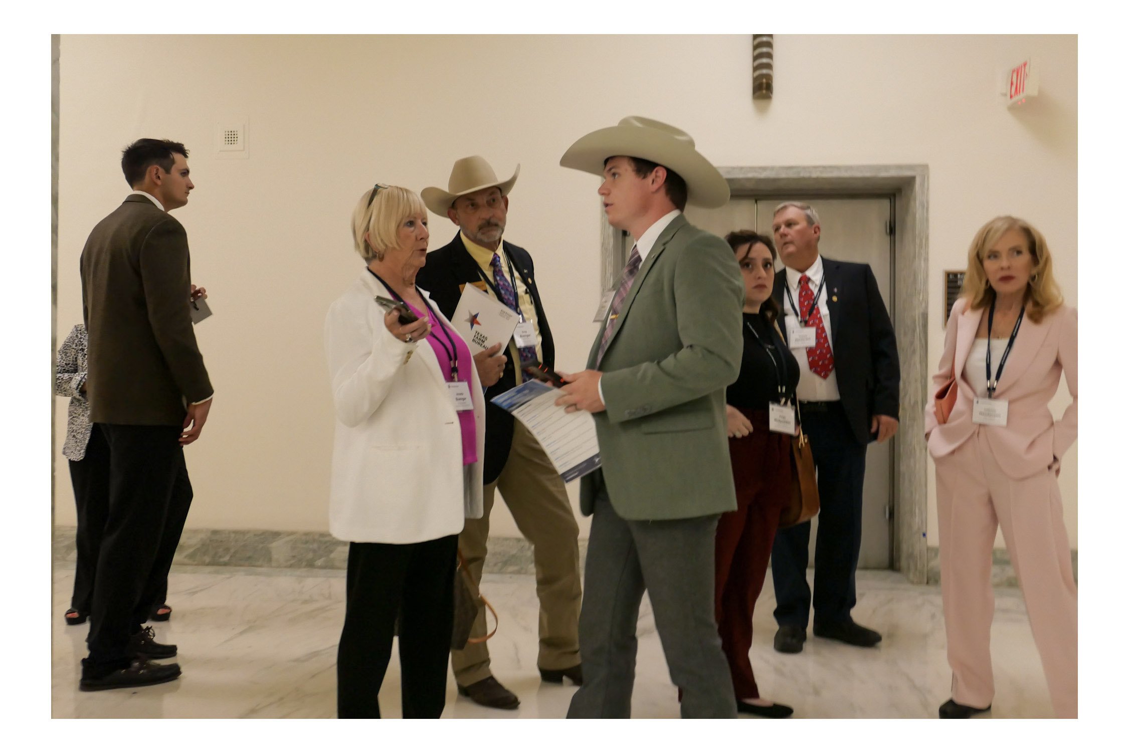 Group of people in conversation at an indoor event, some wearing business attire and cowboy hats.