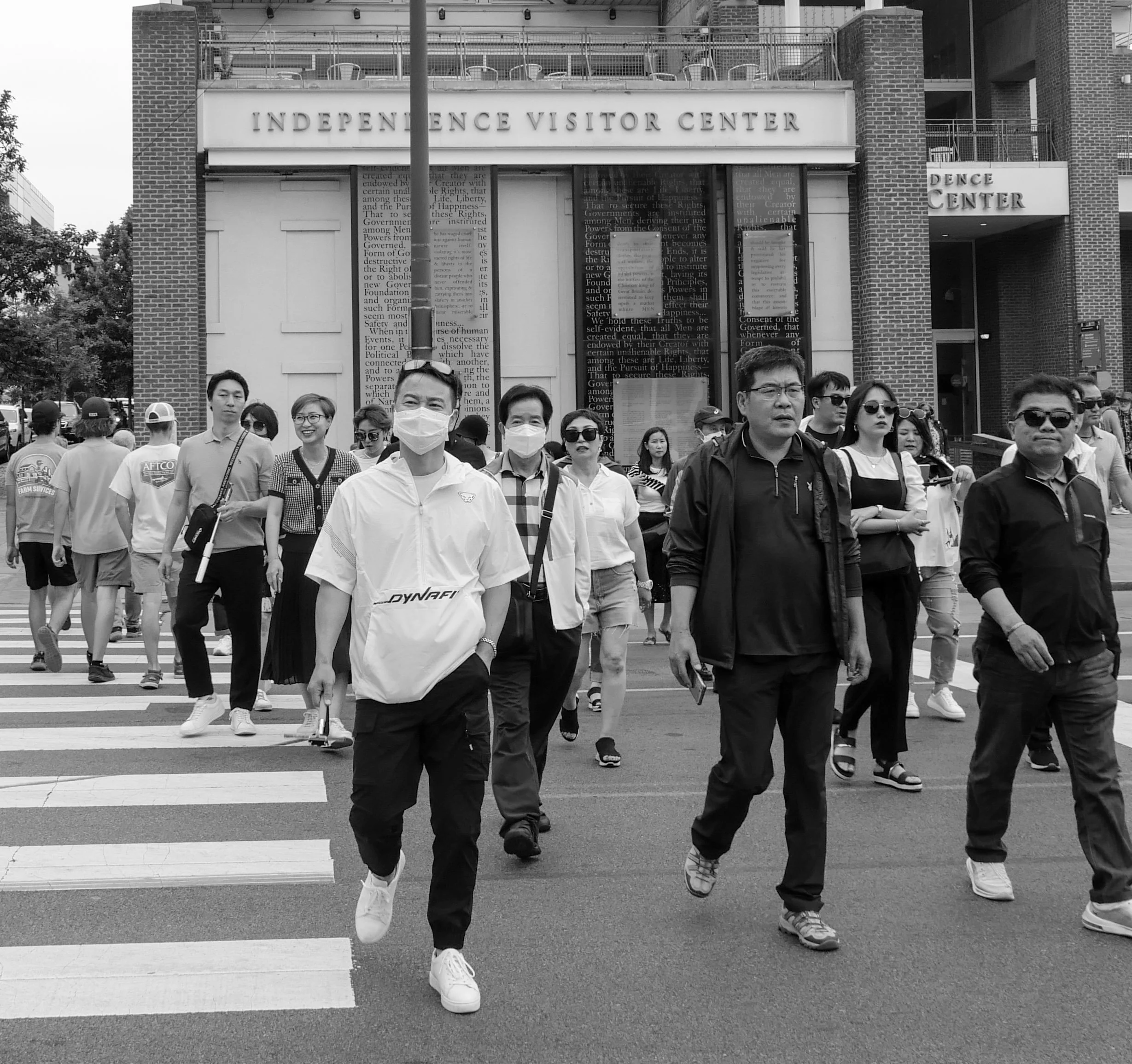 People crossing a street in front of the Independence Visitor Center with some wearing face masks.