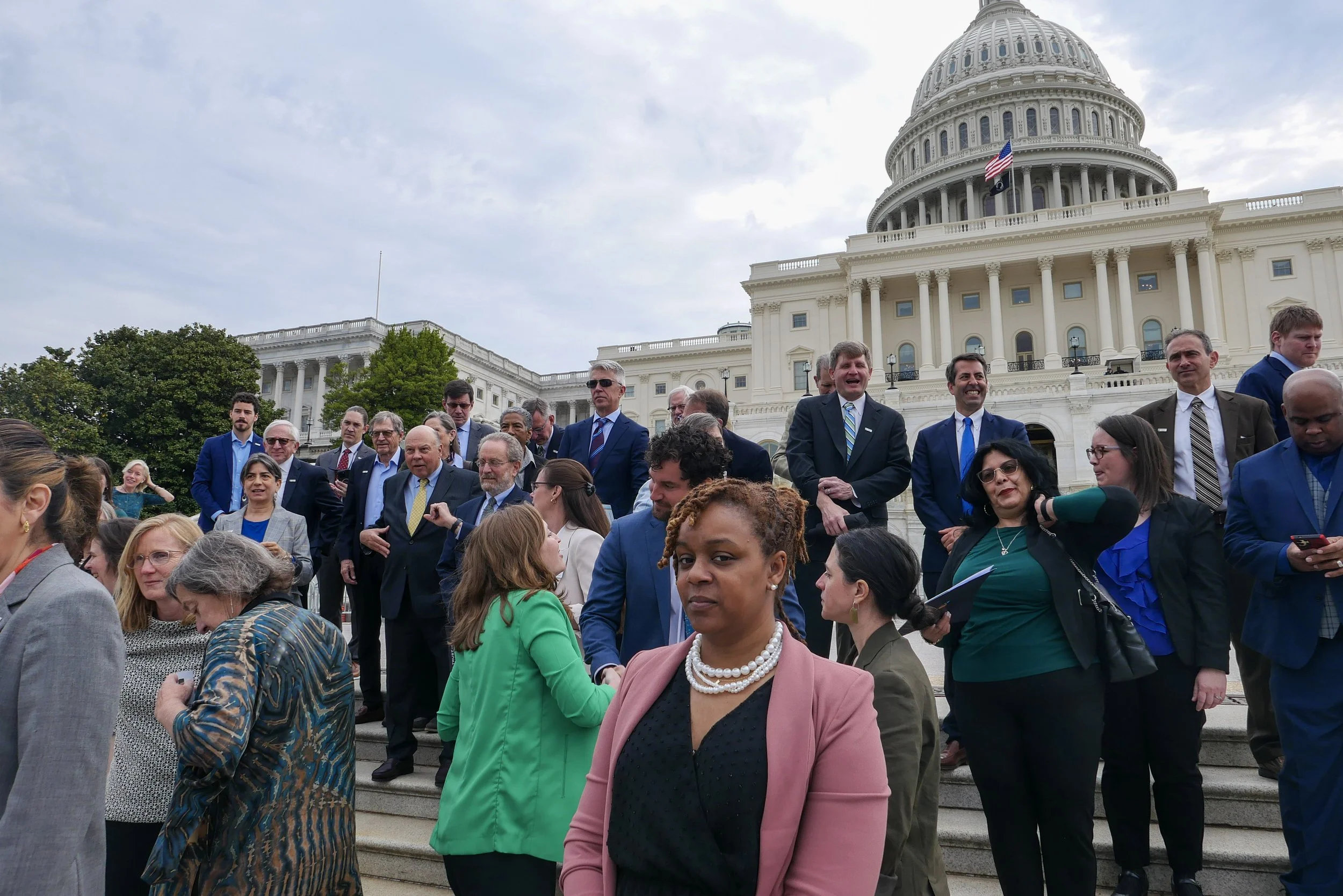 A group of diverse people gathered on the steps of the U.S. Capitol building in Washington D.C. on a cloudy day.