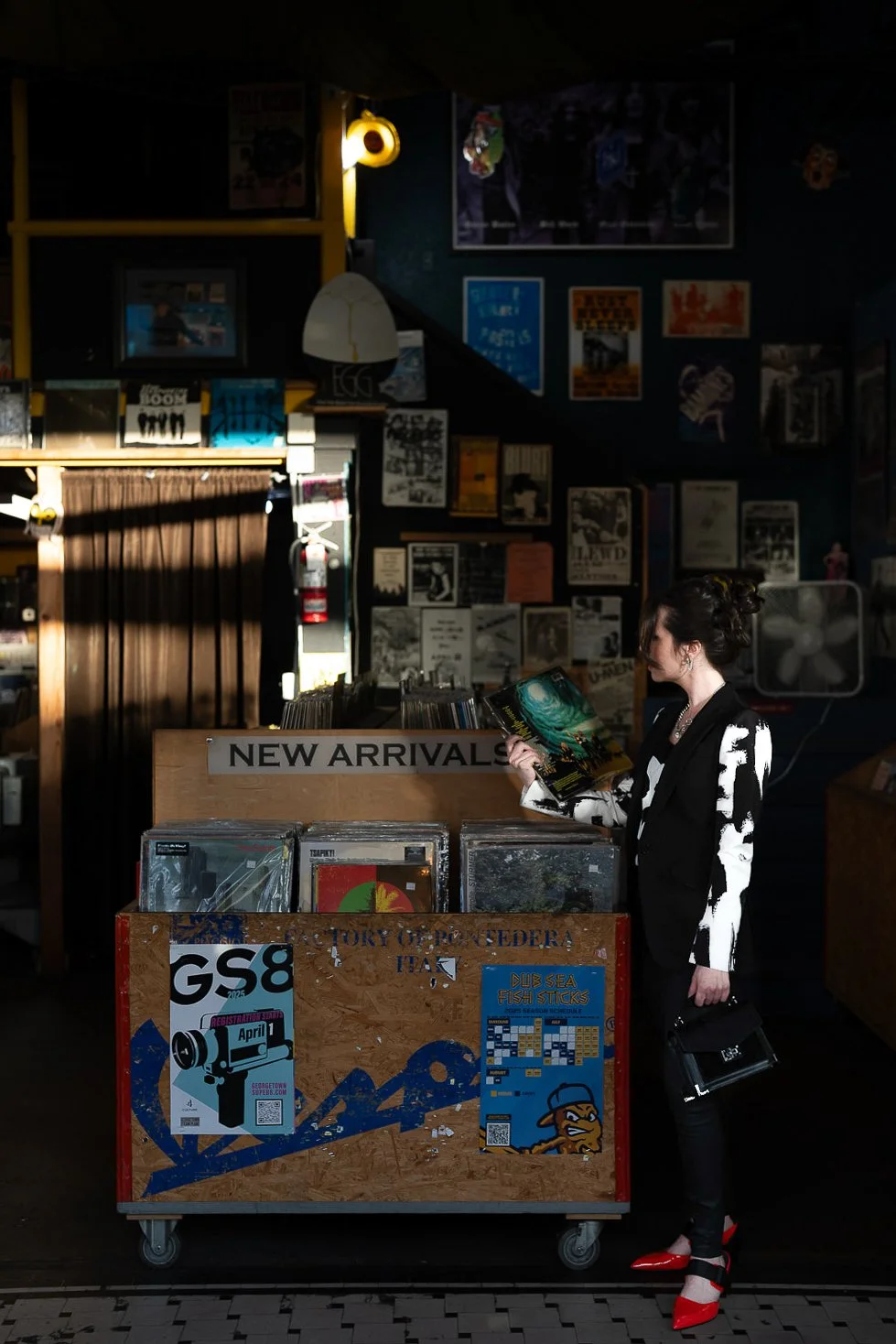 A woman in a black and white outfit with red shoes is standing in a record store, browsing through vinyl records with a