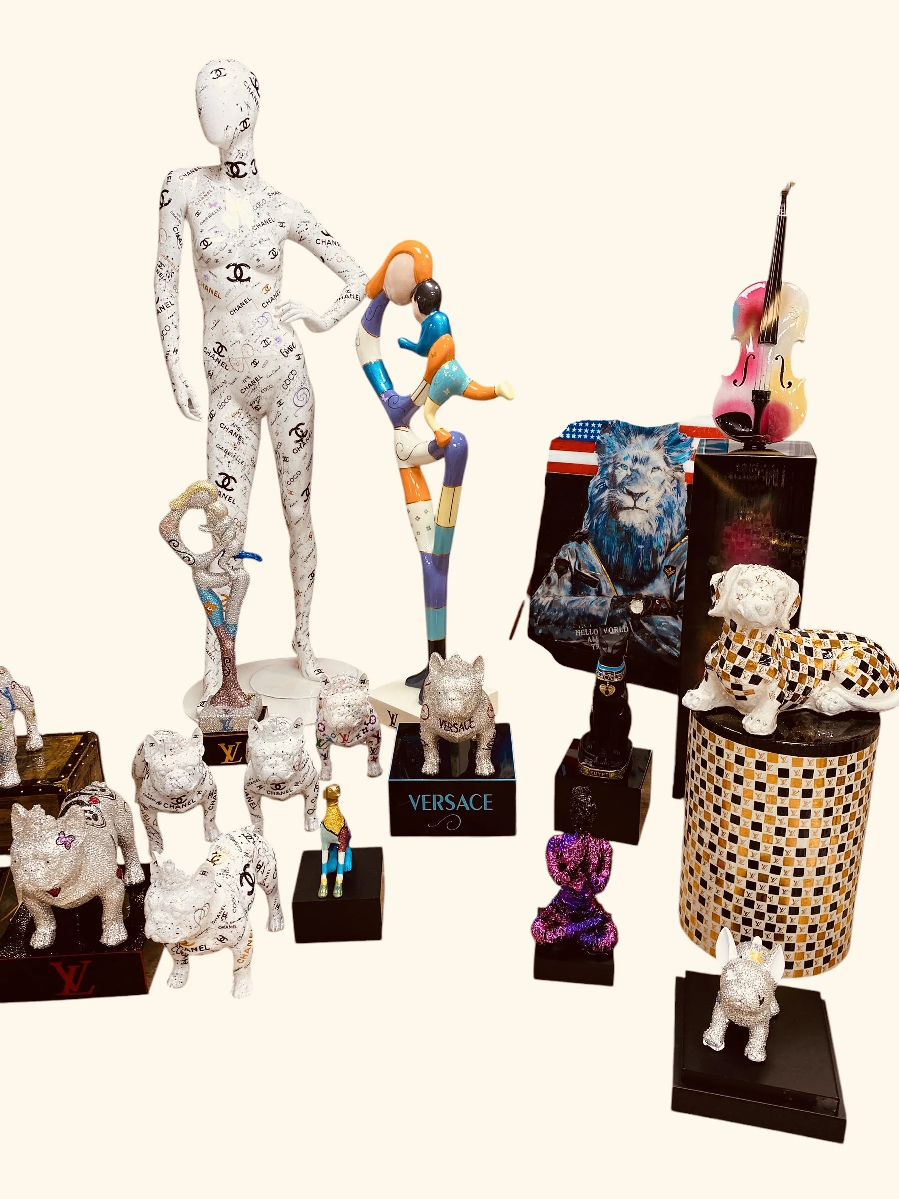 Collection of decorative animal and human figures, including a large white cat with a small white dog figurine, a glittery white dog, a colorful abstract figure, and a Roman soldier. Also features luxury brand items like a I leopard-patterned bust, a violin, and a small gold trophy shaped like a dog.