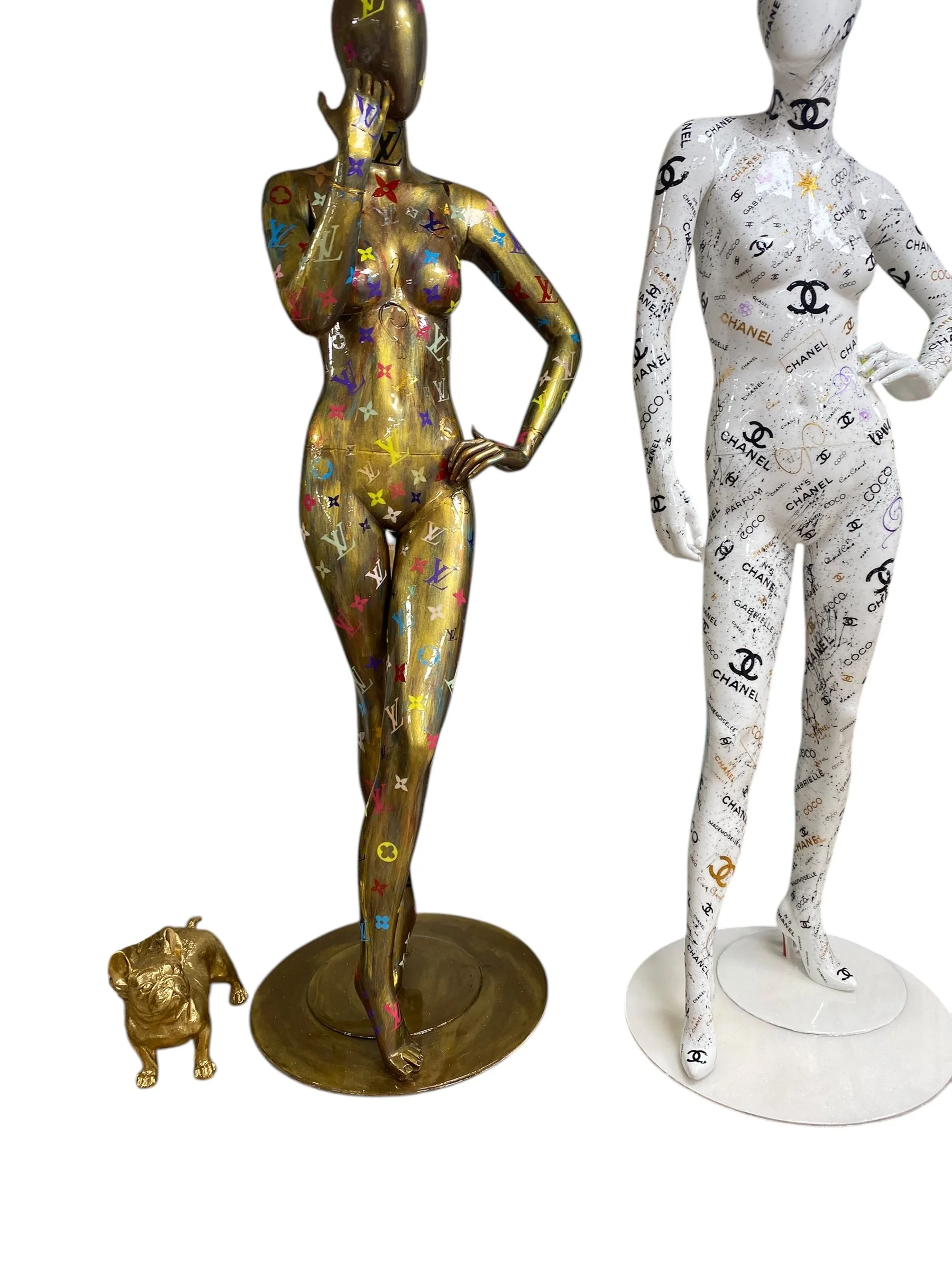 Decorative mannequin figures with Chanel and Louis Vuitton logos, a small gold lion statue, and a gold handbag.