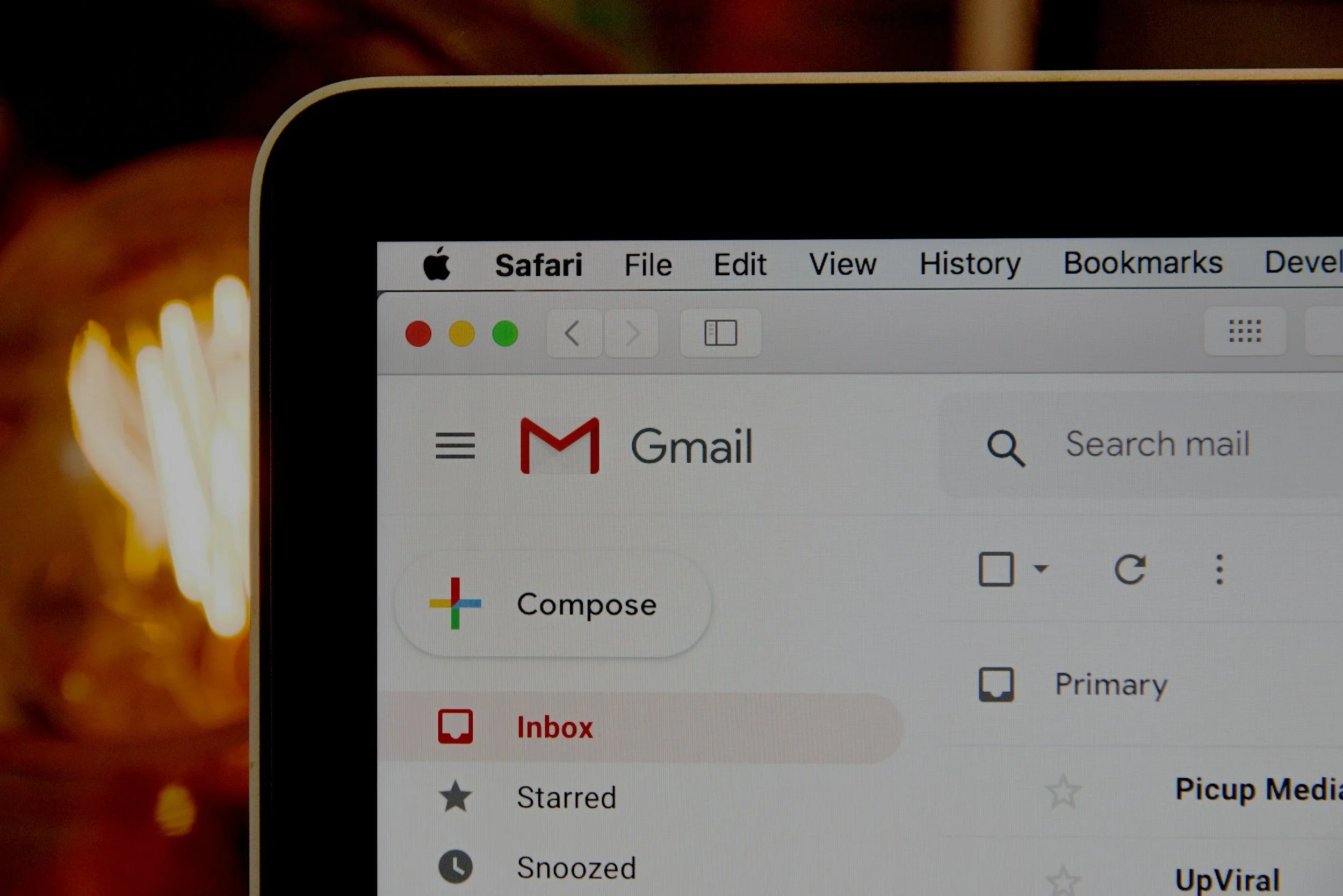 Close-up of a computer screen displaying a Gmail inbox inside Safari web browser on a MacBook. The top menu bar shows options like File, Edit, View, History, Bookmarks, Develop. The email labels and icons for inbox, starred, snoozed, and others are visible.