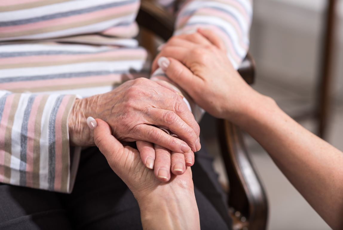 Two people holding hands, one appears to be elderly with wrinkled skin and the other younger with smoother skin.