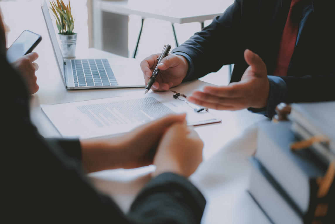 Two people in a business meeting discussing documents, with a laptop and smartphone on the table.