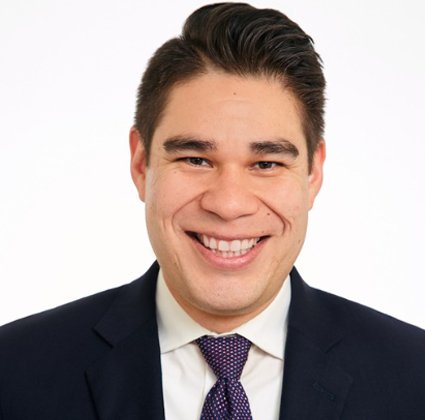 Smiling man in a suit and tie with dark hair and light skin.