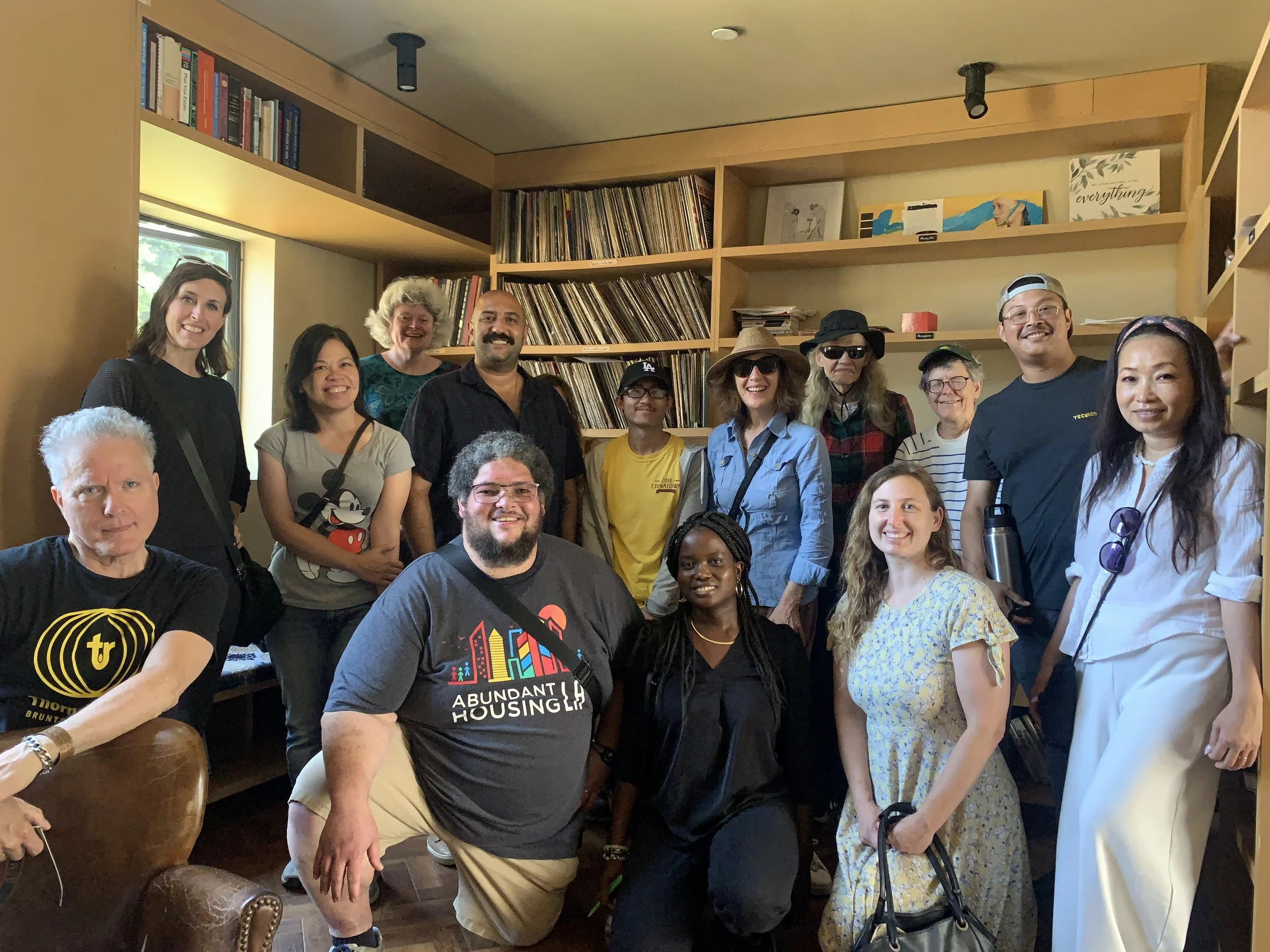 Group of diverse people smiling and posing together indoors, with bookshelves filled with books and vinyl records in the background.