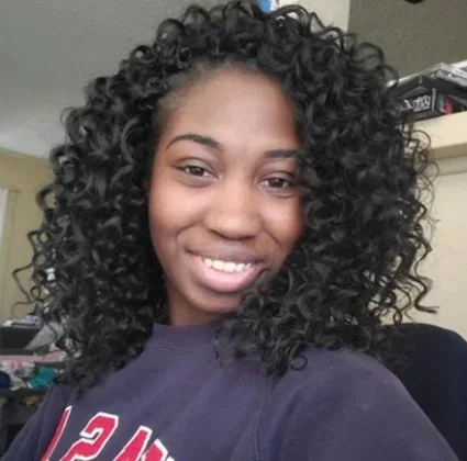 Young woman with curly black hair smiling in an indoor setting.