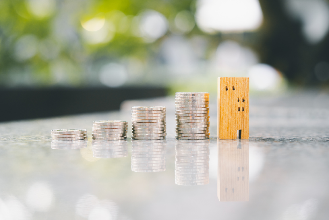 Stacks of coins arranged in increasing order, with a wooden block with holes resembling a face, on a reflective surface outdoors.