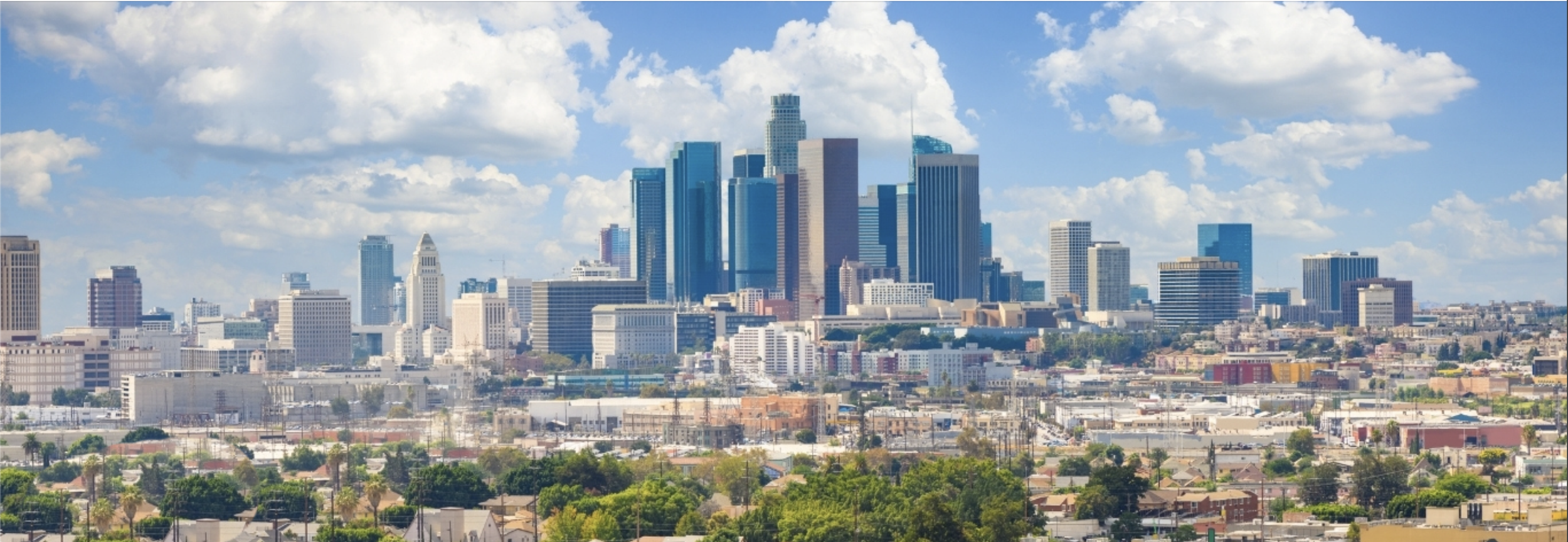 Panoramic view of downtown Los Angeles with tall skyscrapers against a blue sky with clouds.