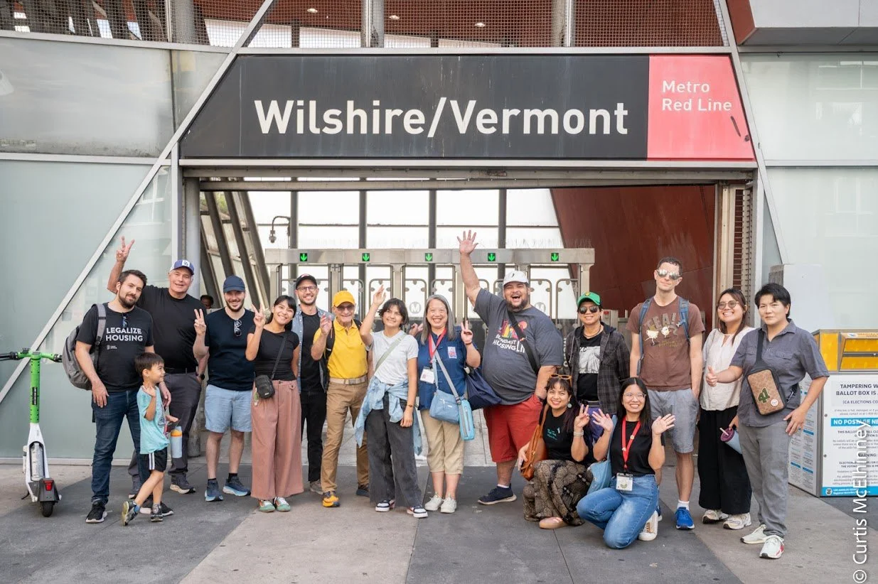 Group of people in front of Wilshire/Vermont metro station, with smiles and peace signs, posing for a photo on a city sidewalk.