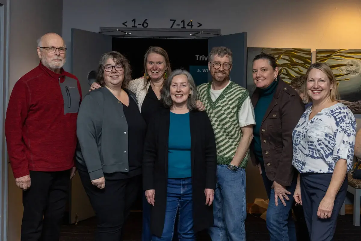 Group of seven people standing together indoors, smiling for the camera.