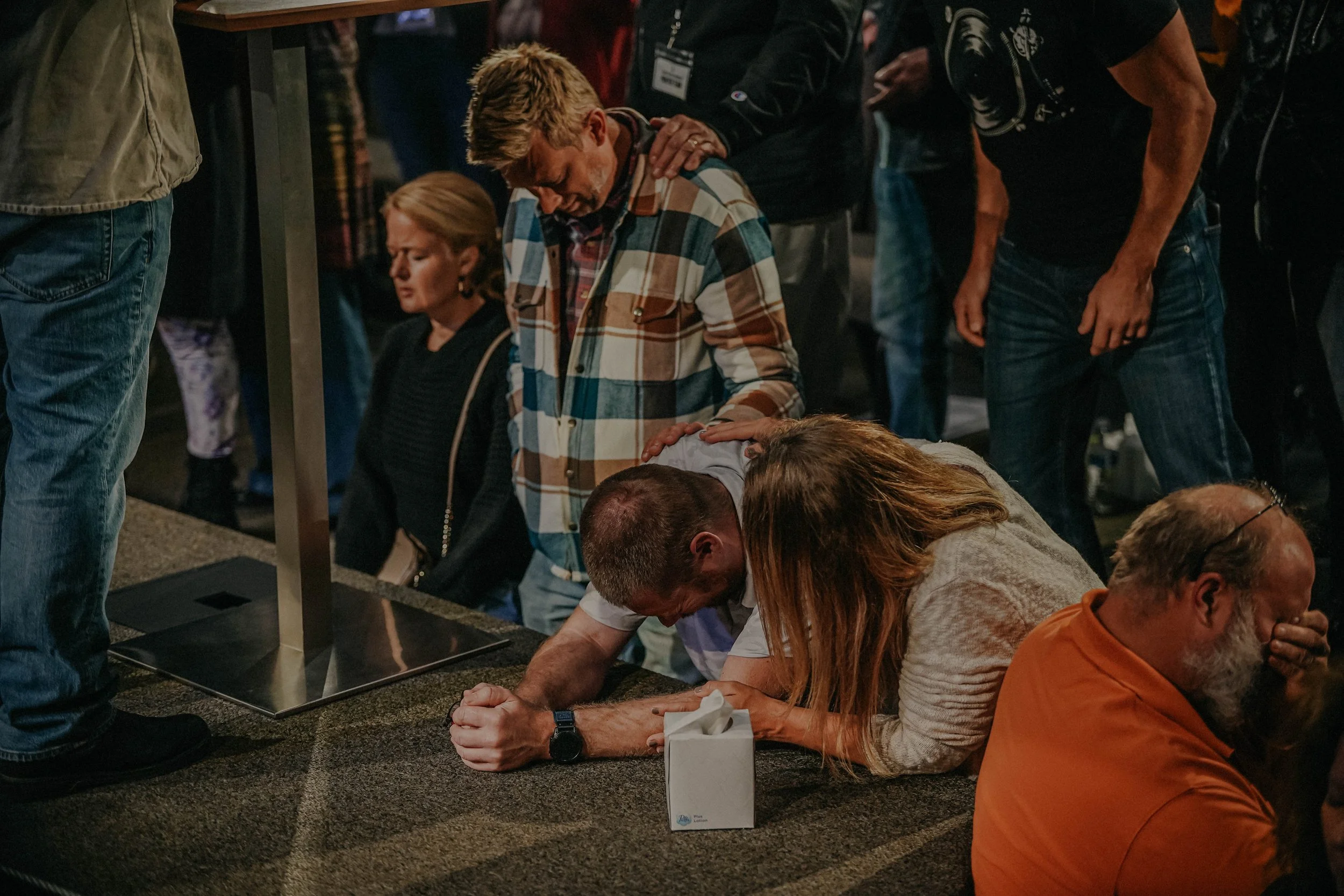 Group of people kneeling and praying during a religious gathering, with some holding hands and heads bowed.