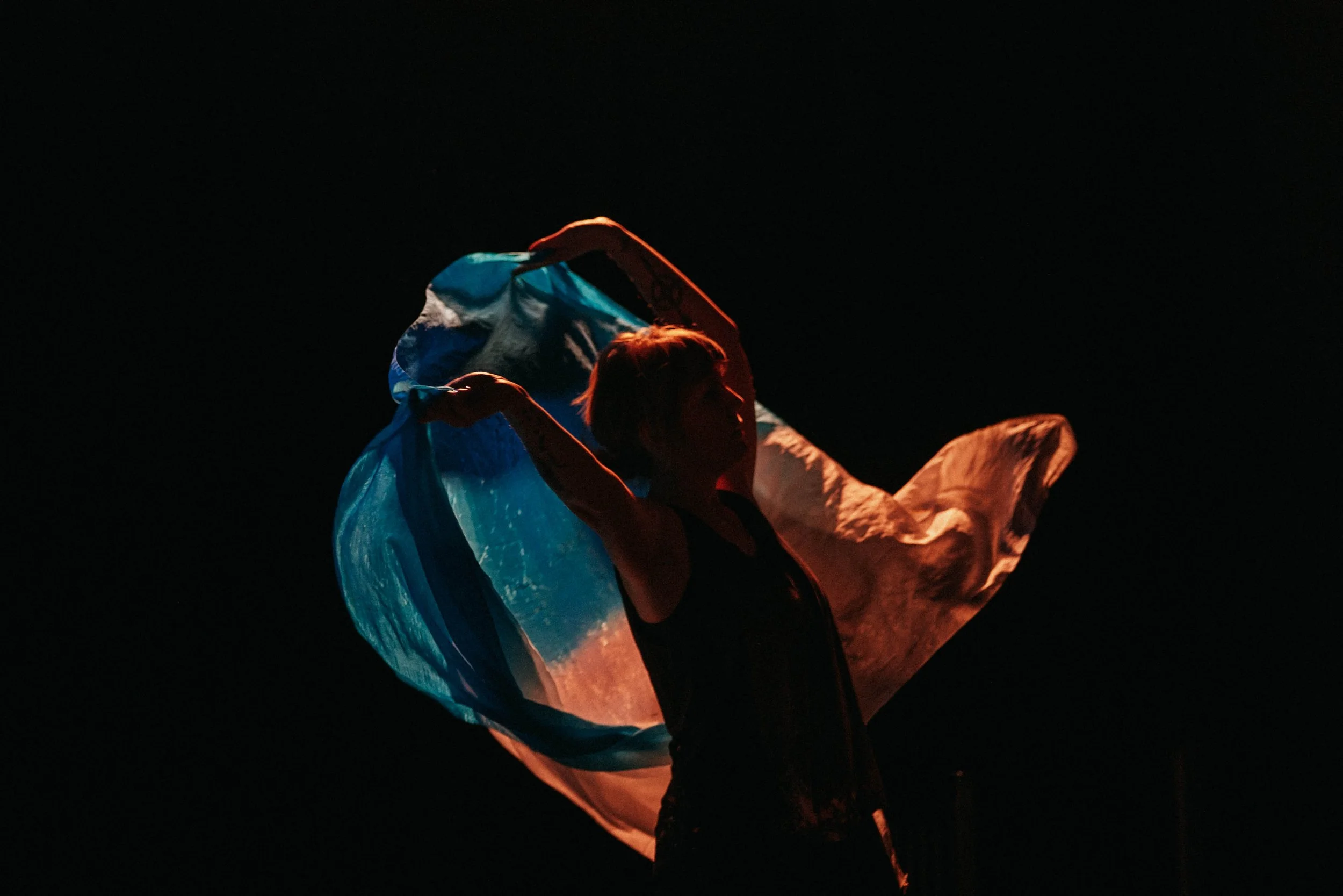 Person holding a colorful, illuminated fabric or scarf against a dark background, creating a vibrant and dramatic visual effect.