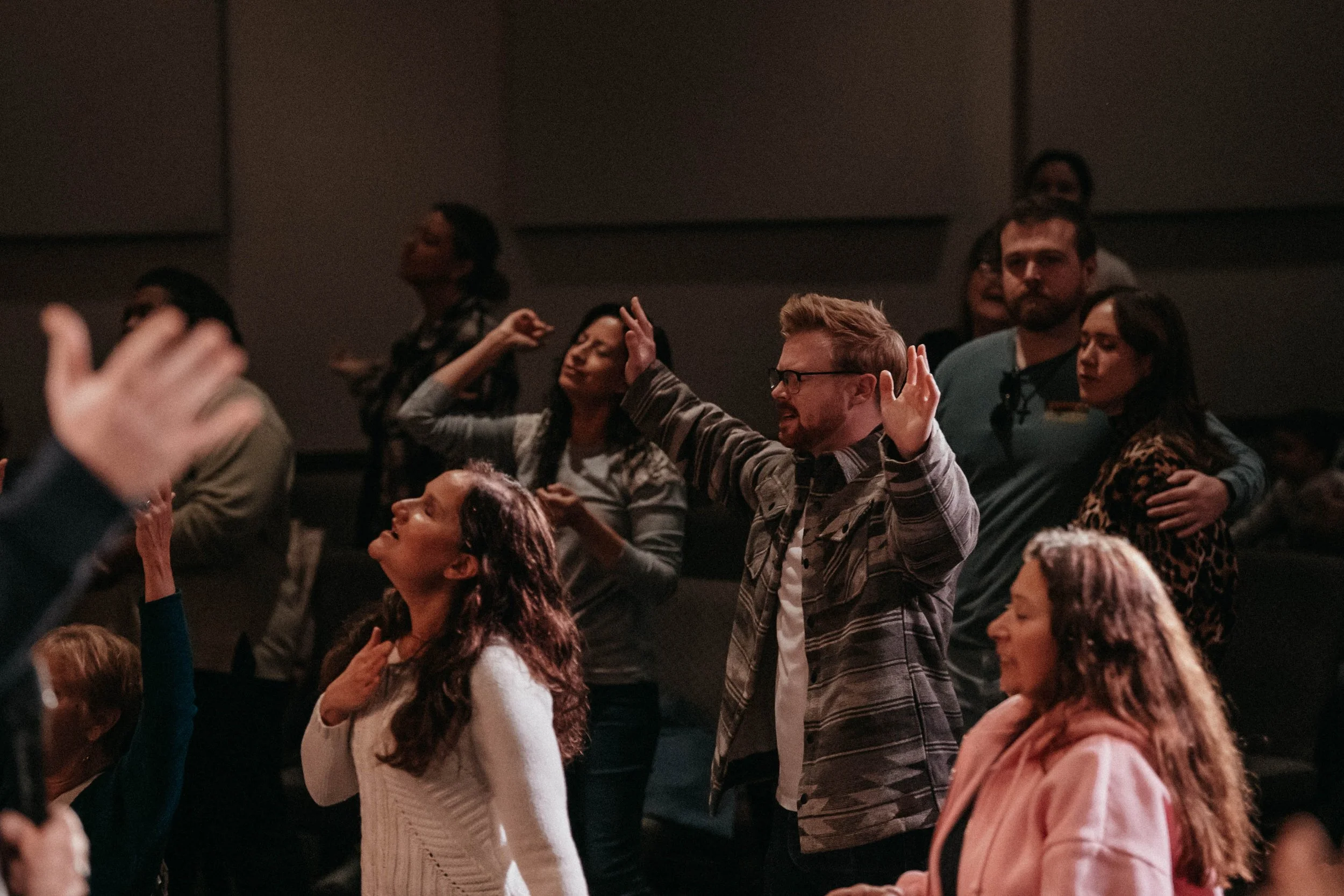 A diverse group of people with closed eyes and raised hands participating in a religious or spiritual gathering.