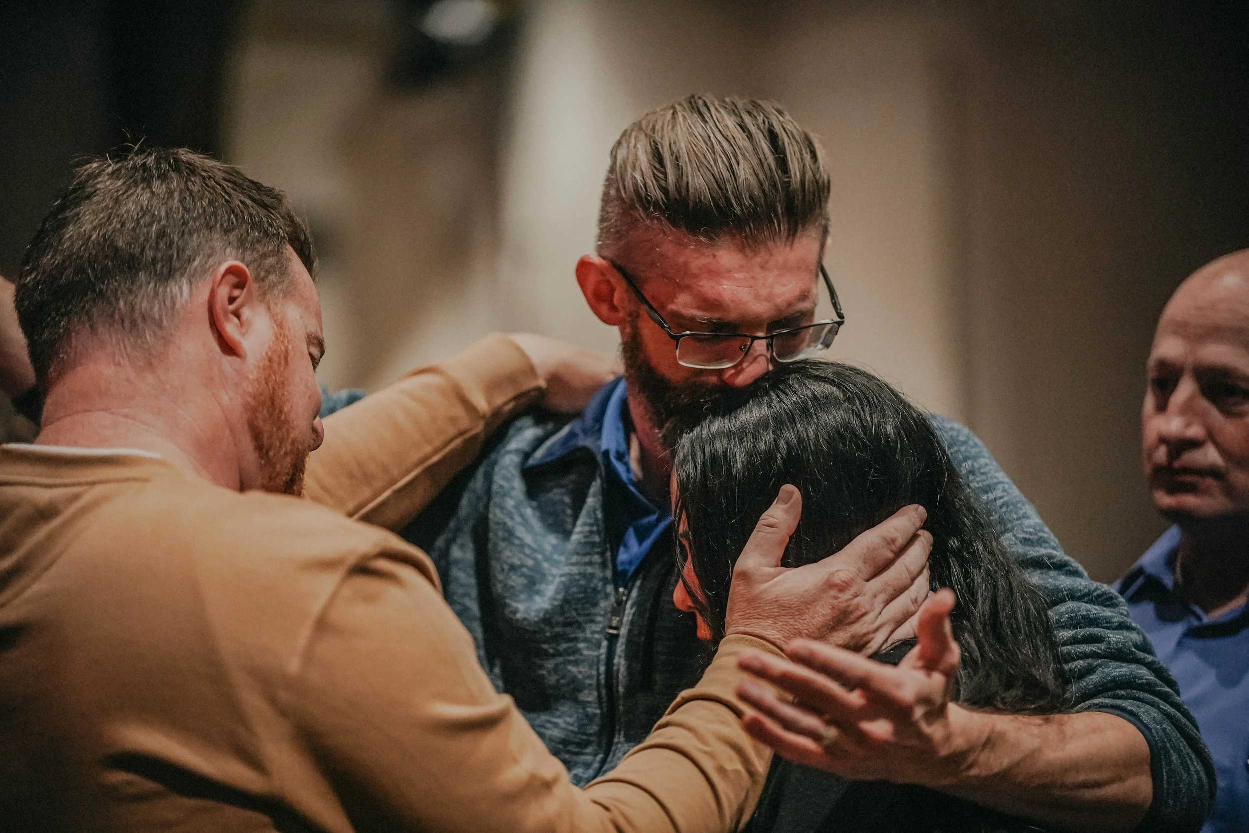 Group of people embracing and praying together in a moment of connection.