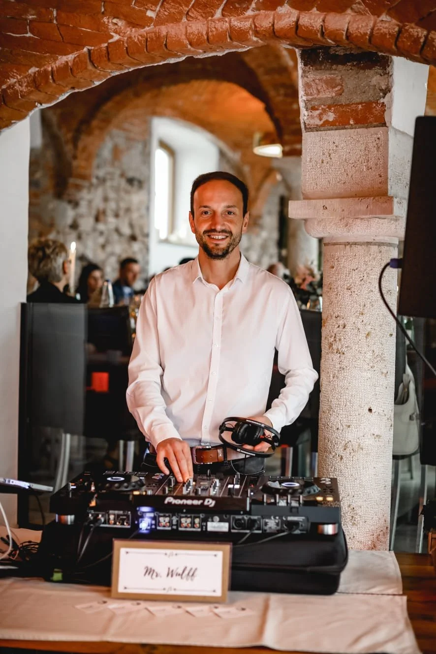 Hochzeits-DJ am Pult im Gewölbekeller, umgeben von feiernden Gästen