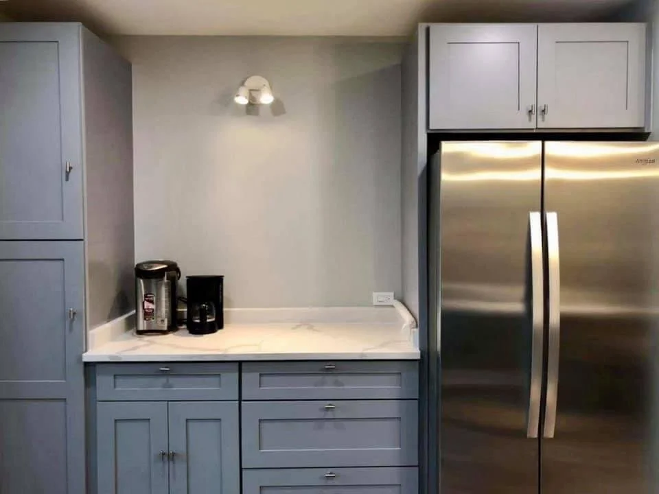 Kitchen corner with gray cabinets, a marble countertop, a refrigerator, and a coffee maker.