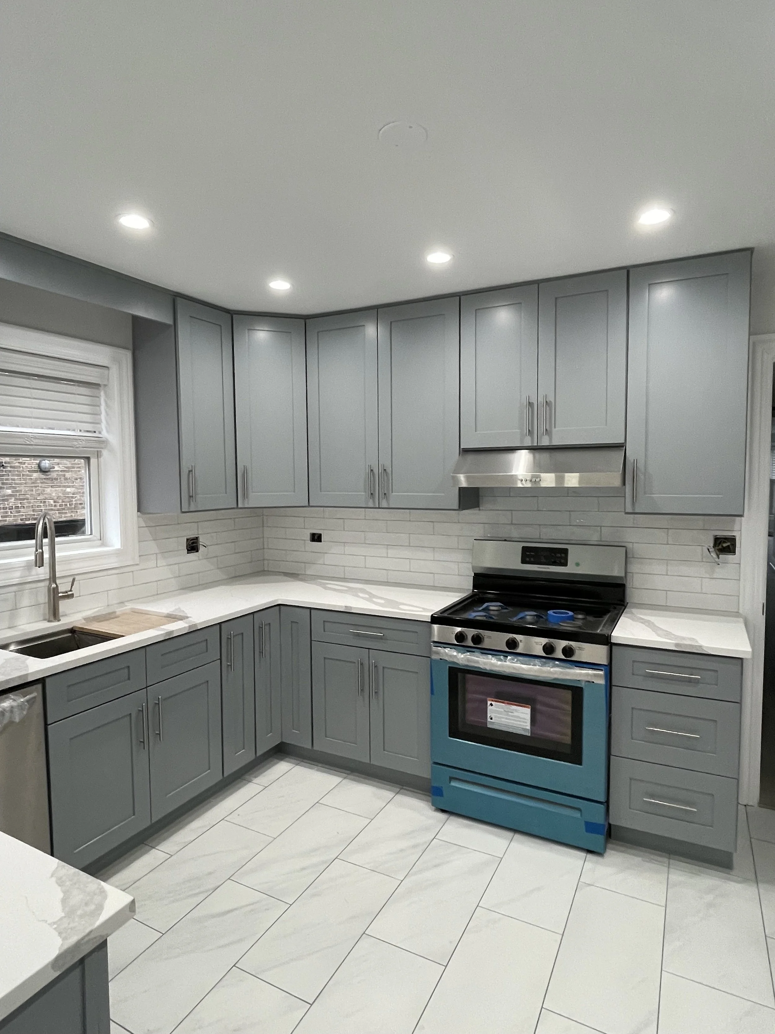Modern kitchen with gray cabinets, white marble countertops, stainless steel oven, and recessed lighting.
