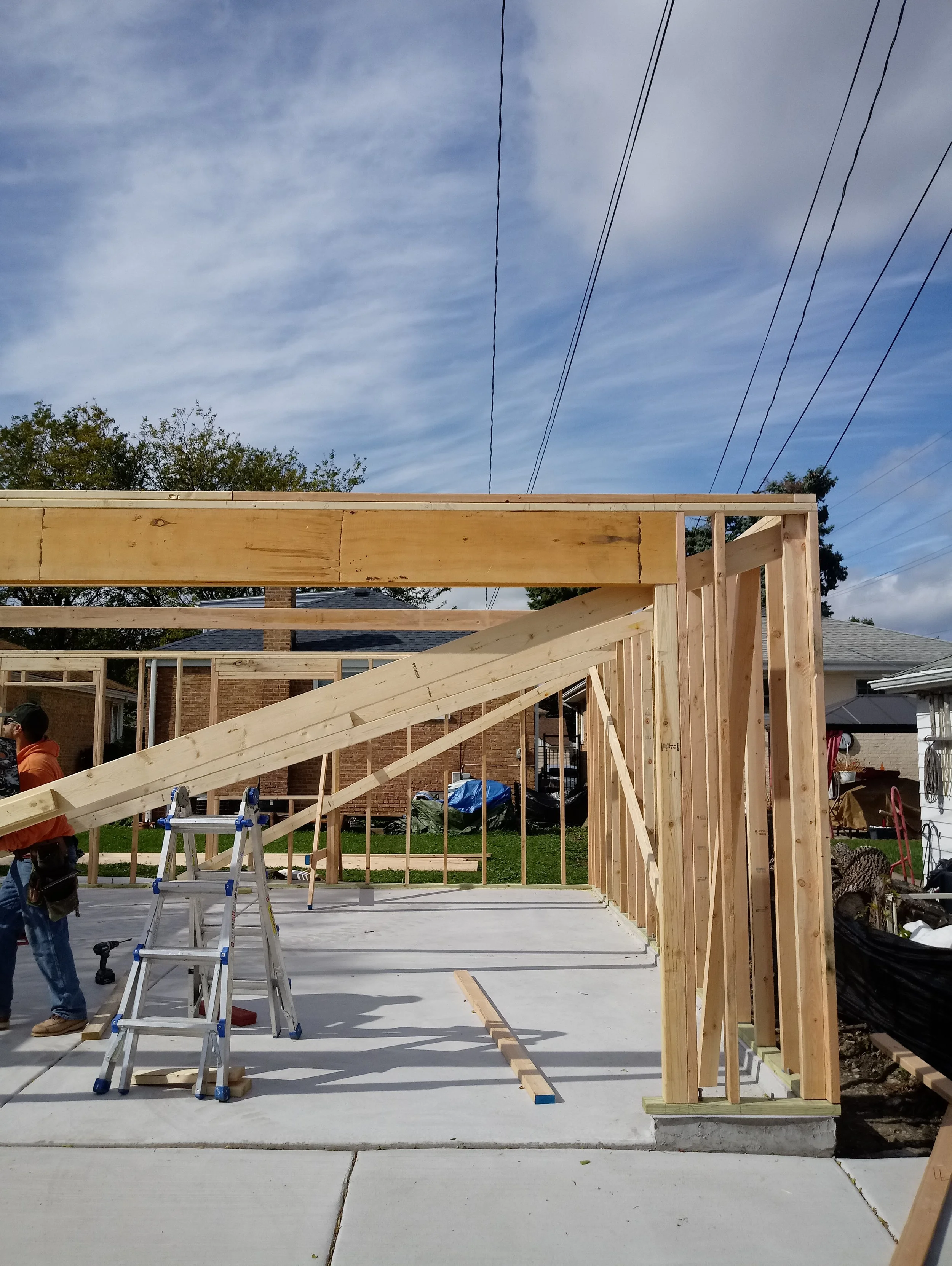 Construction site with wooden framing for a building, construction workers, ladders, tools, and a clear sky with some clouds.