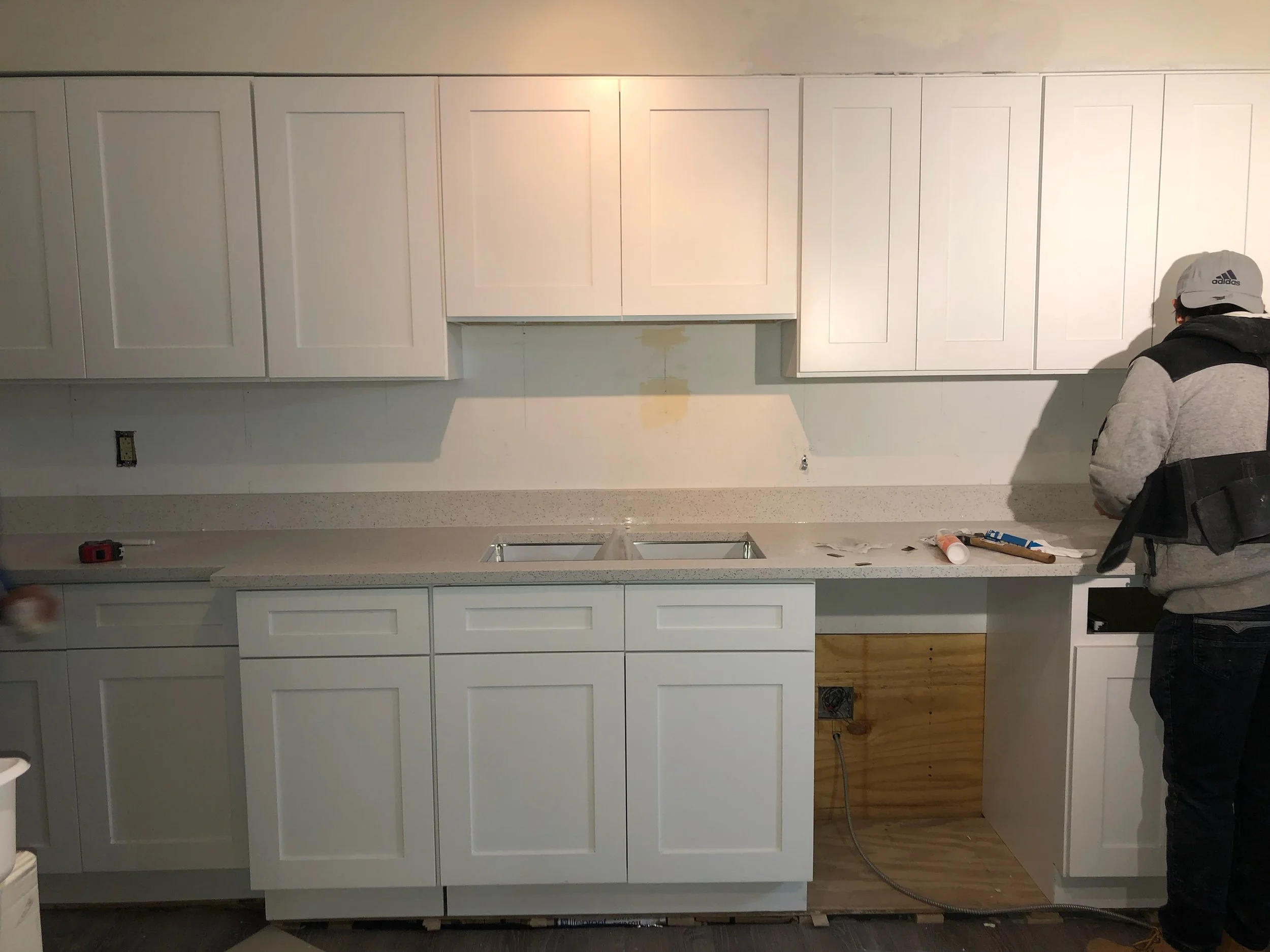 Construction worker installing white kitchen cabinets with some tools and materials on the countertop.