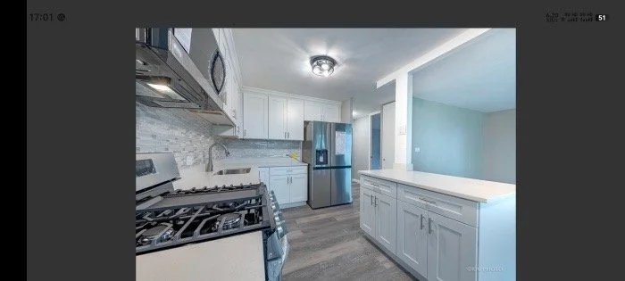 Kitchen with white cabinets, stainless steel appliances, gray backsplash, and hardwood flooring.