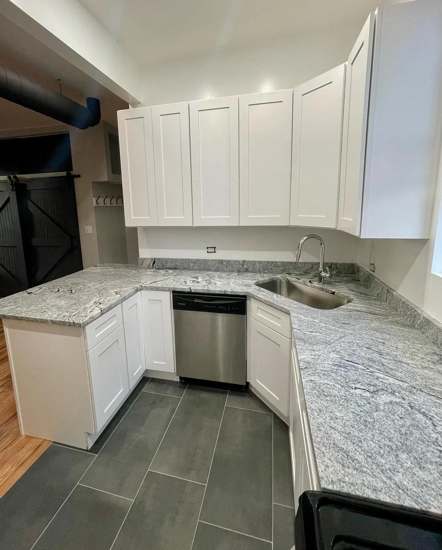 Modern kitchen with white cabinets, gray granite countertops, stainless steel sink, and dishwasher, with black tiled floor.