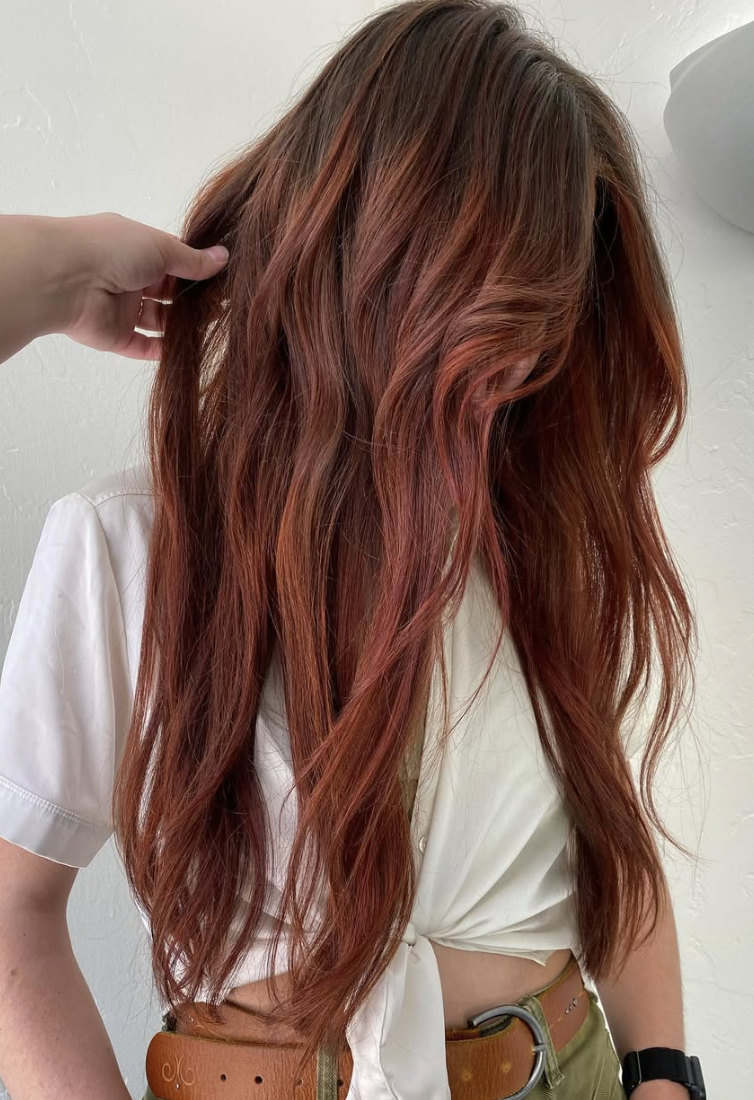 A person with long, wavy red hair, wearing a white tied-up shirt and a brown belt.