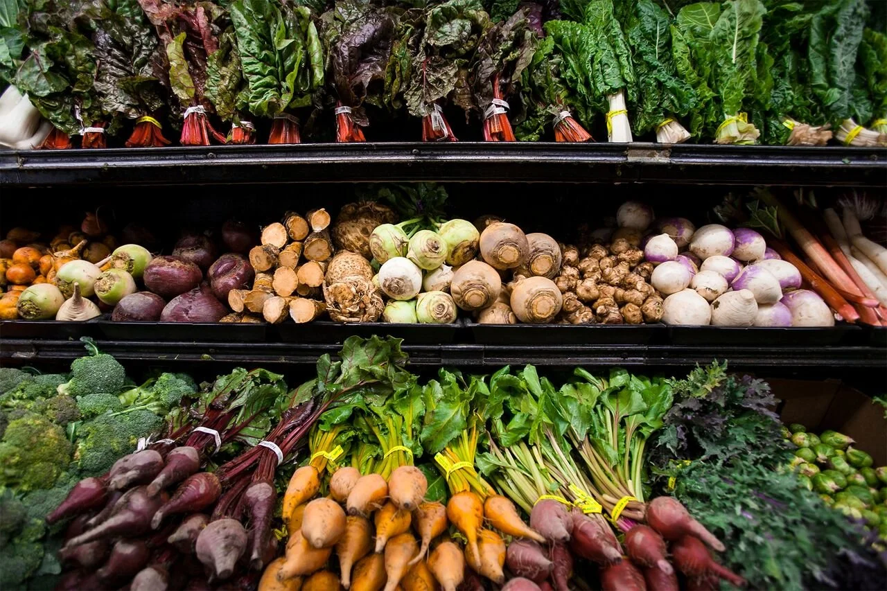 Display of fresh vegetables at a grocery store, including carrots, radishes, broccoli, and leafy greens.