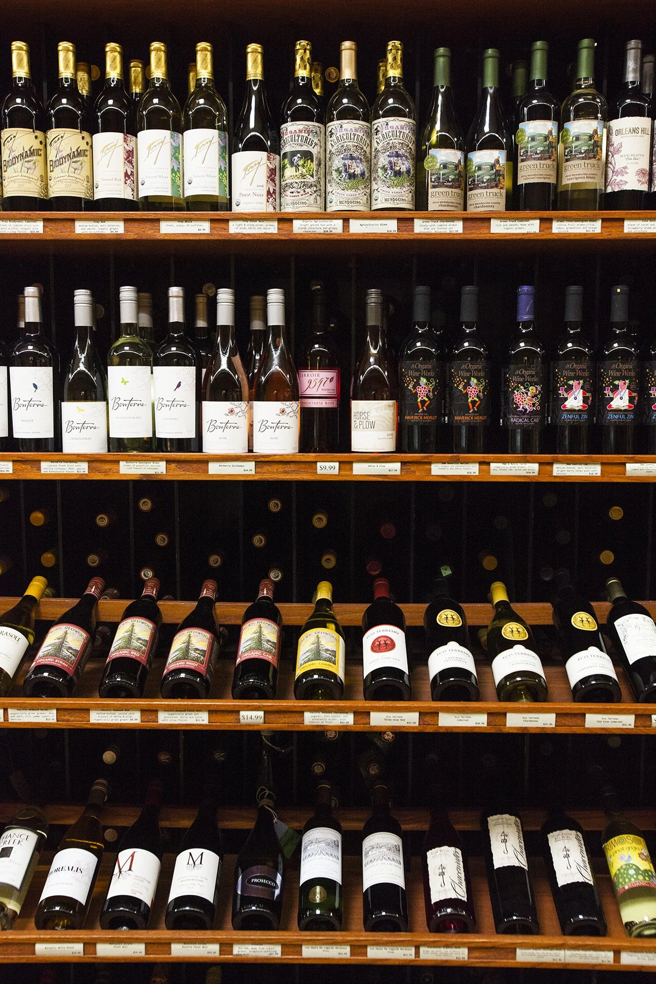 Shelves lined with various bottles of wine, including red, white, and rosé, arranged by type and brand in a wine store.