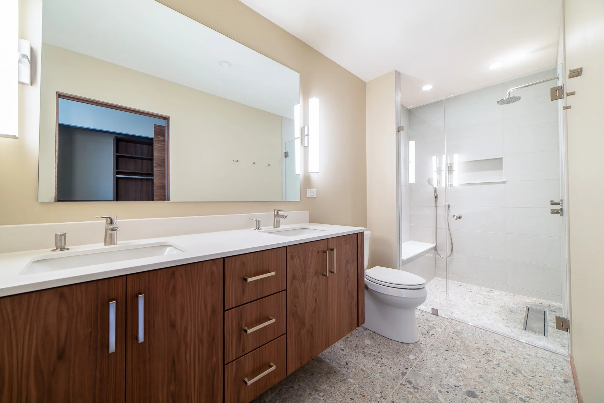 Modern bathroom with double vanity sink, large mirror, walk-in shower with glass door, and beige walls.