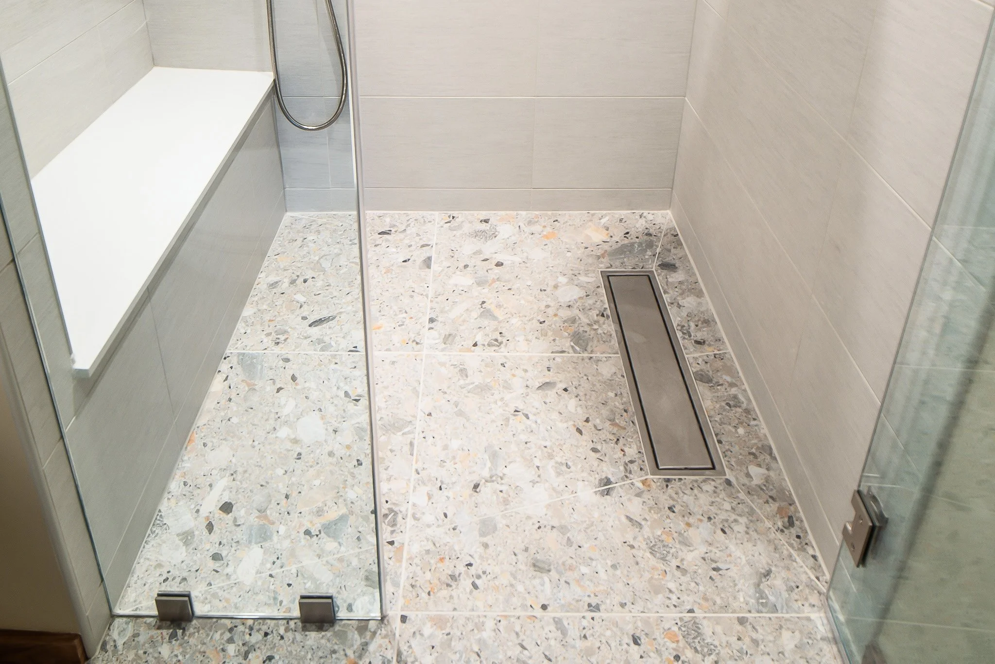 Photo of a modern shower with glass walls, terrazzo floor, gray tiled walls, a built-in shelf, and a linear drain.