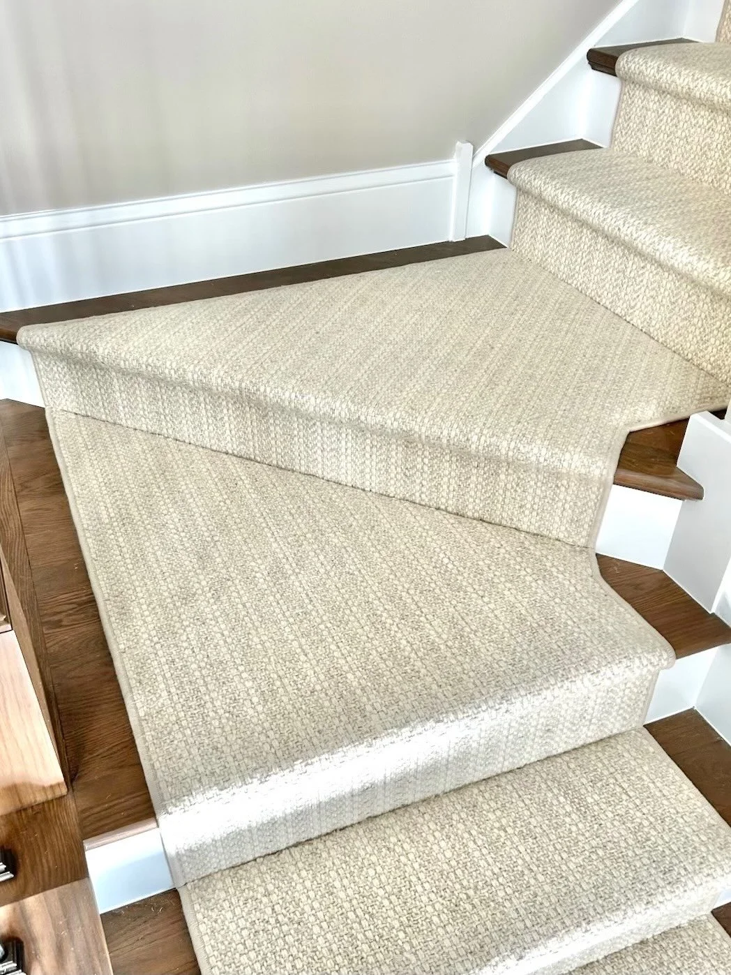 Carpeted stairs with beige carpet and wooden steps, showing a stair lift chair in an indoor setting.