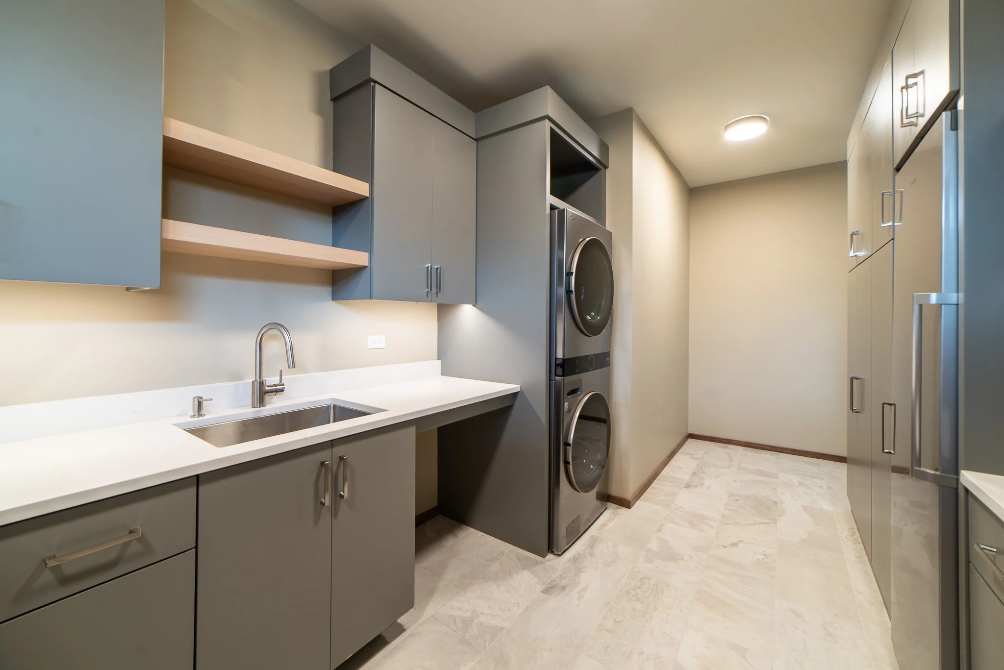 Modern laundry room with gray cabinets, a white countertop with a sink, and a stacked washer and dryer in stainless steel.