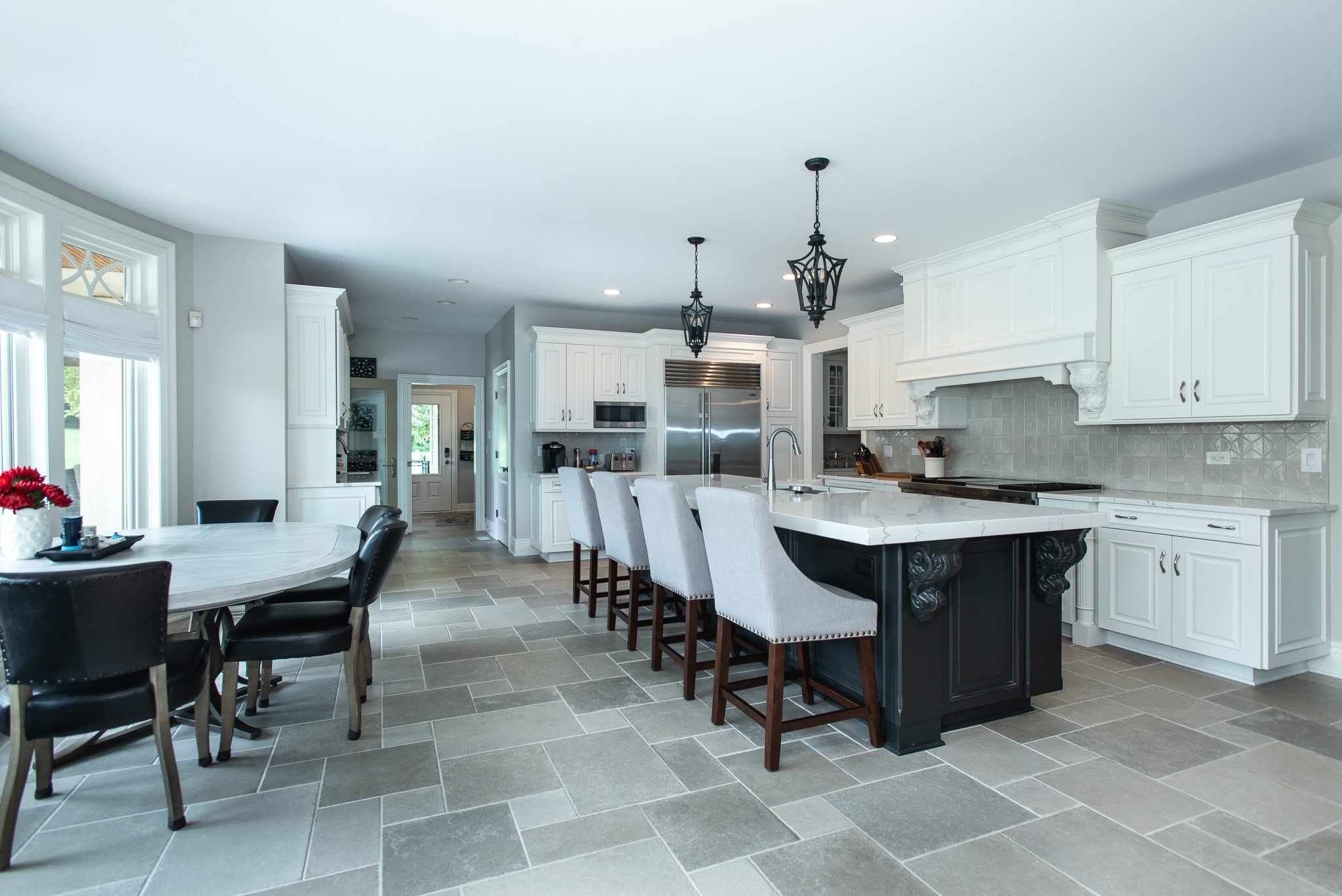 Modern kitchen with white cabinetry, grey tiled floor, black pendant lights, and a white island with beige upholstered chairs.