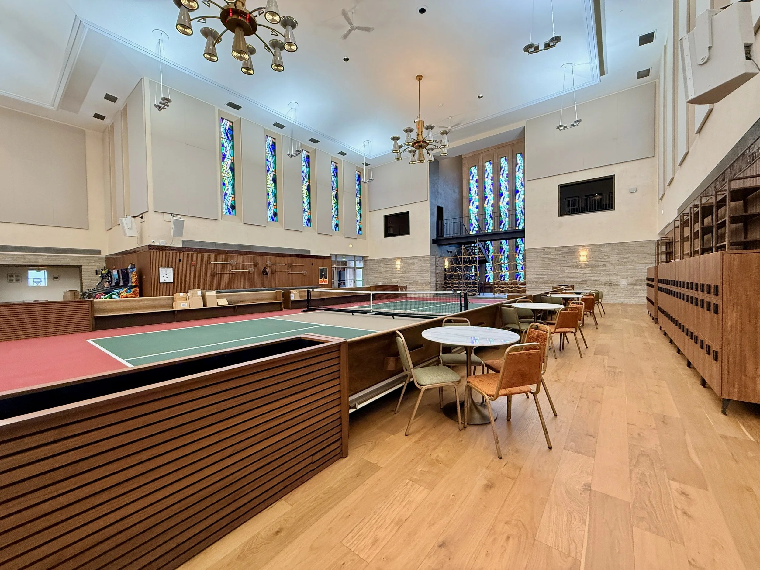 Interior view of a room with high ceilings, stained glass windows, modern chandeliers, and antique-style chairs and tables.