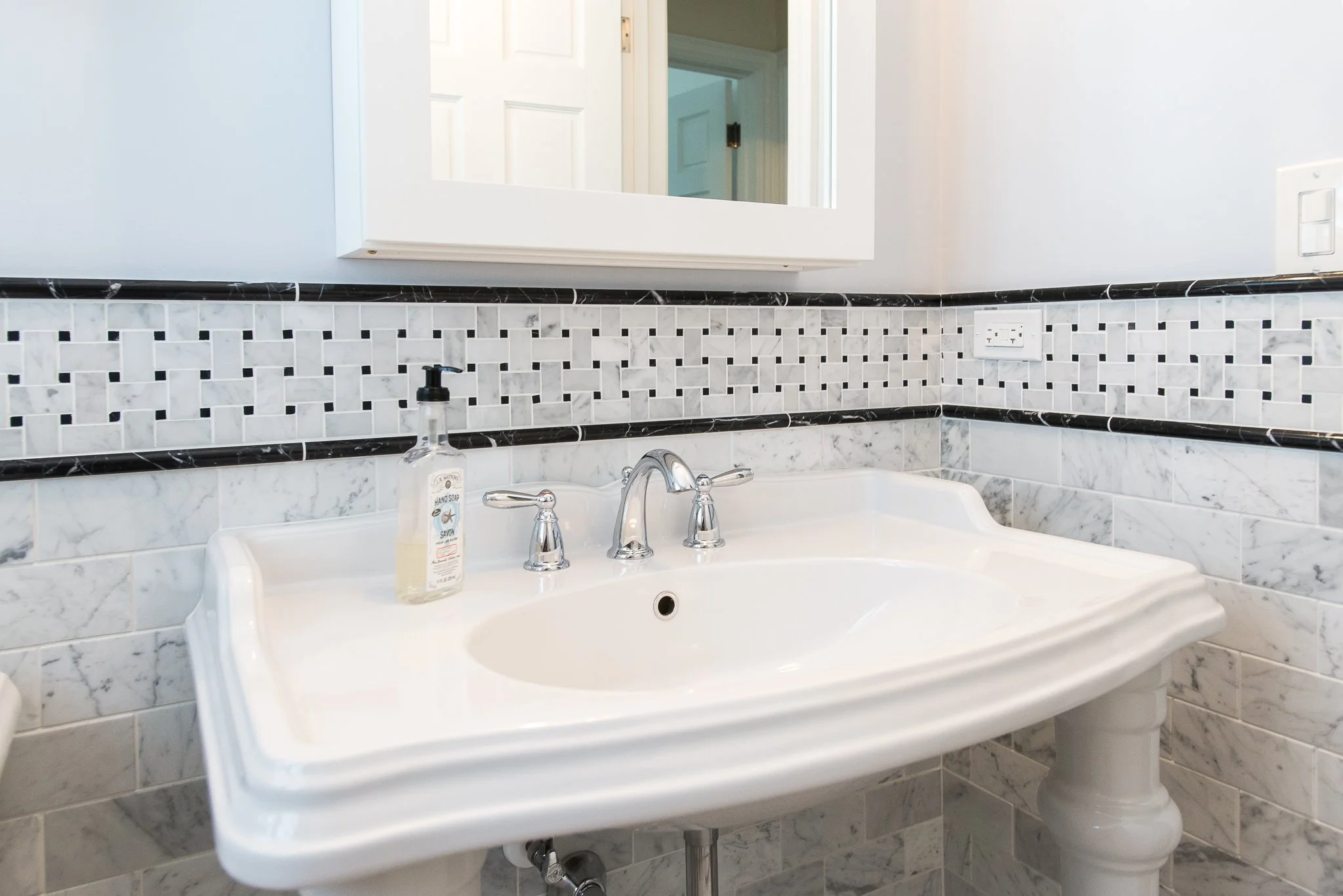 Bathroom sink with marble tile backsplash, a mirror, a soap dispenser, and a faucet.