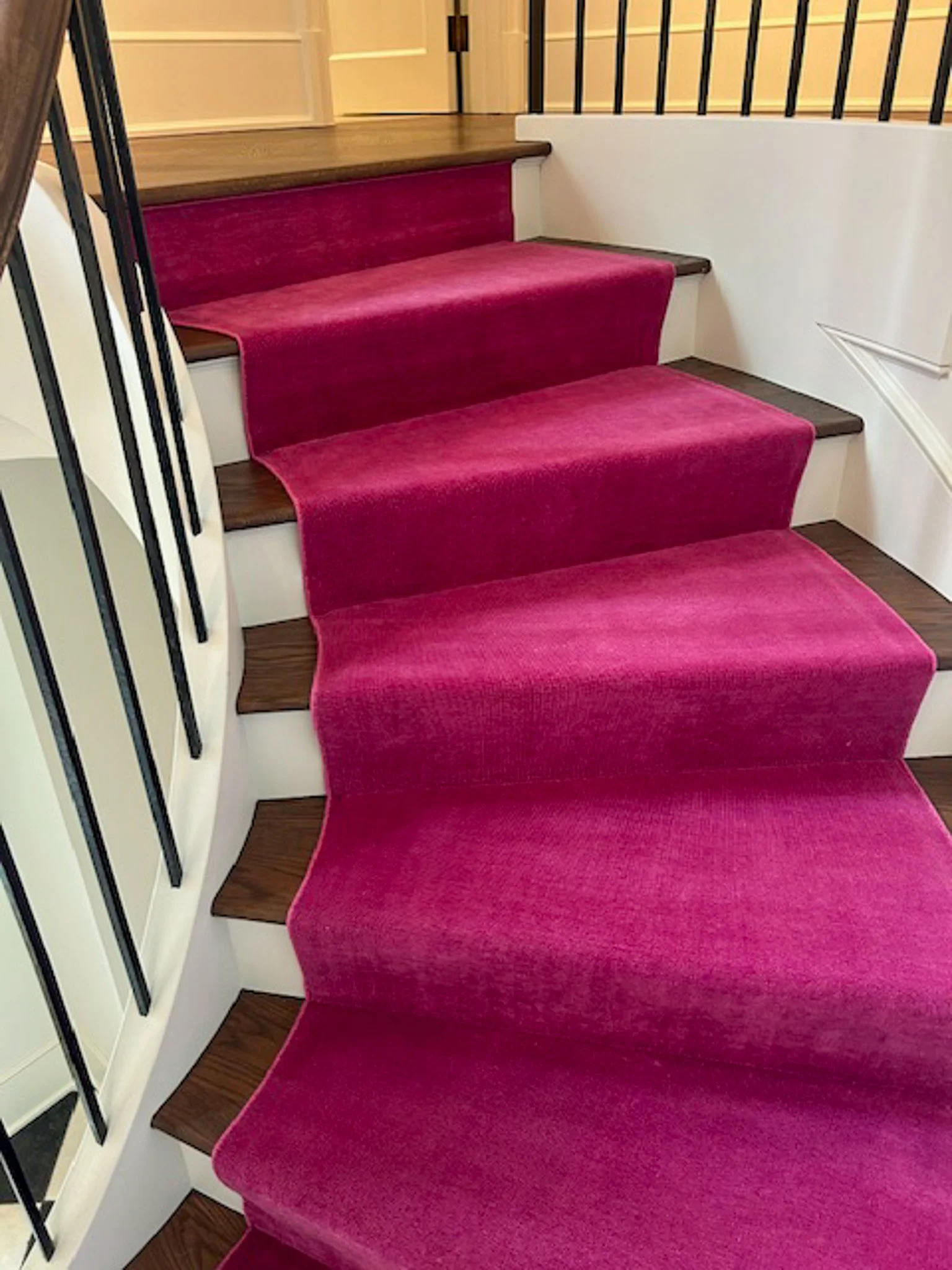 Red carpeted staircase with black metal railing on the left and white wall on the right.